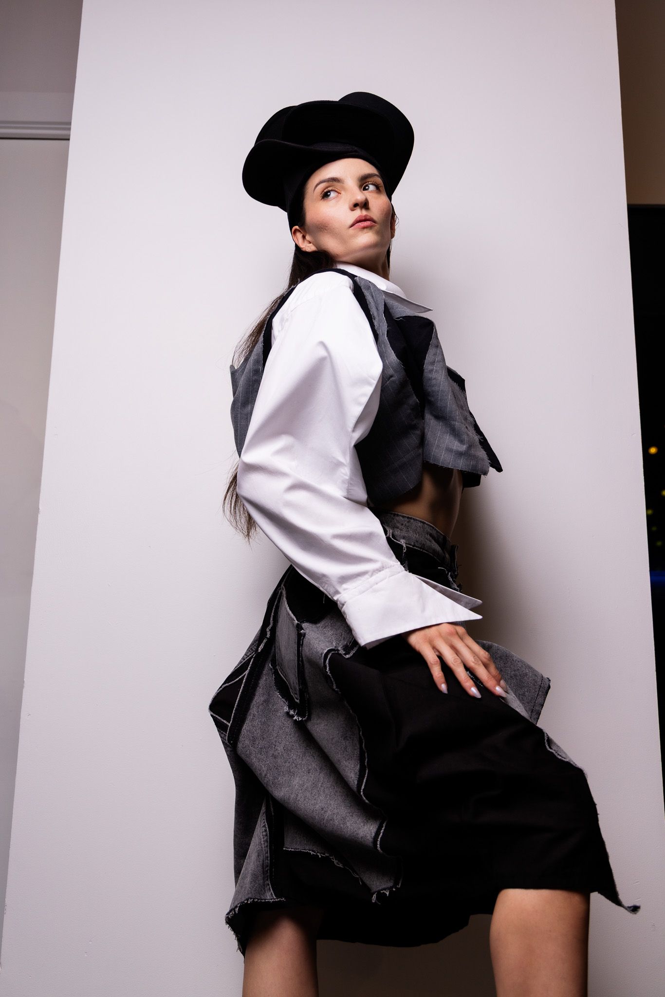 Fashion model in black and white menswear-inspired outfit with beret poses against white wall.