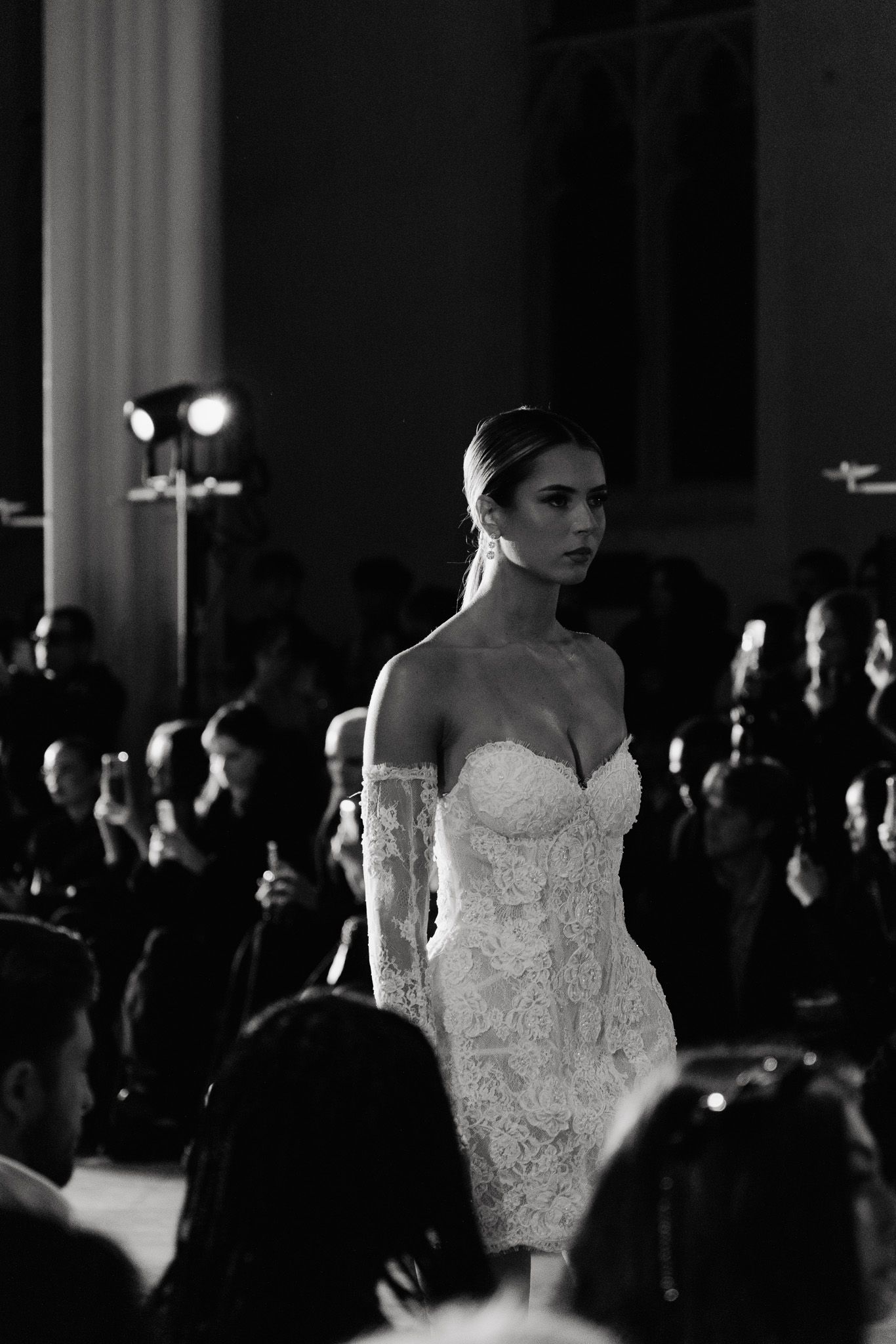 Elegant bridal fashion show featuring white wedding gowns on runway with audience in background.