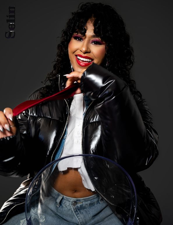 Studio portrait featuring shiny black leather jacket and joyful expression against dark background.