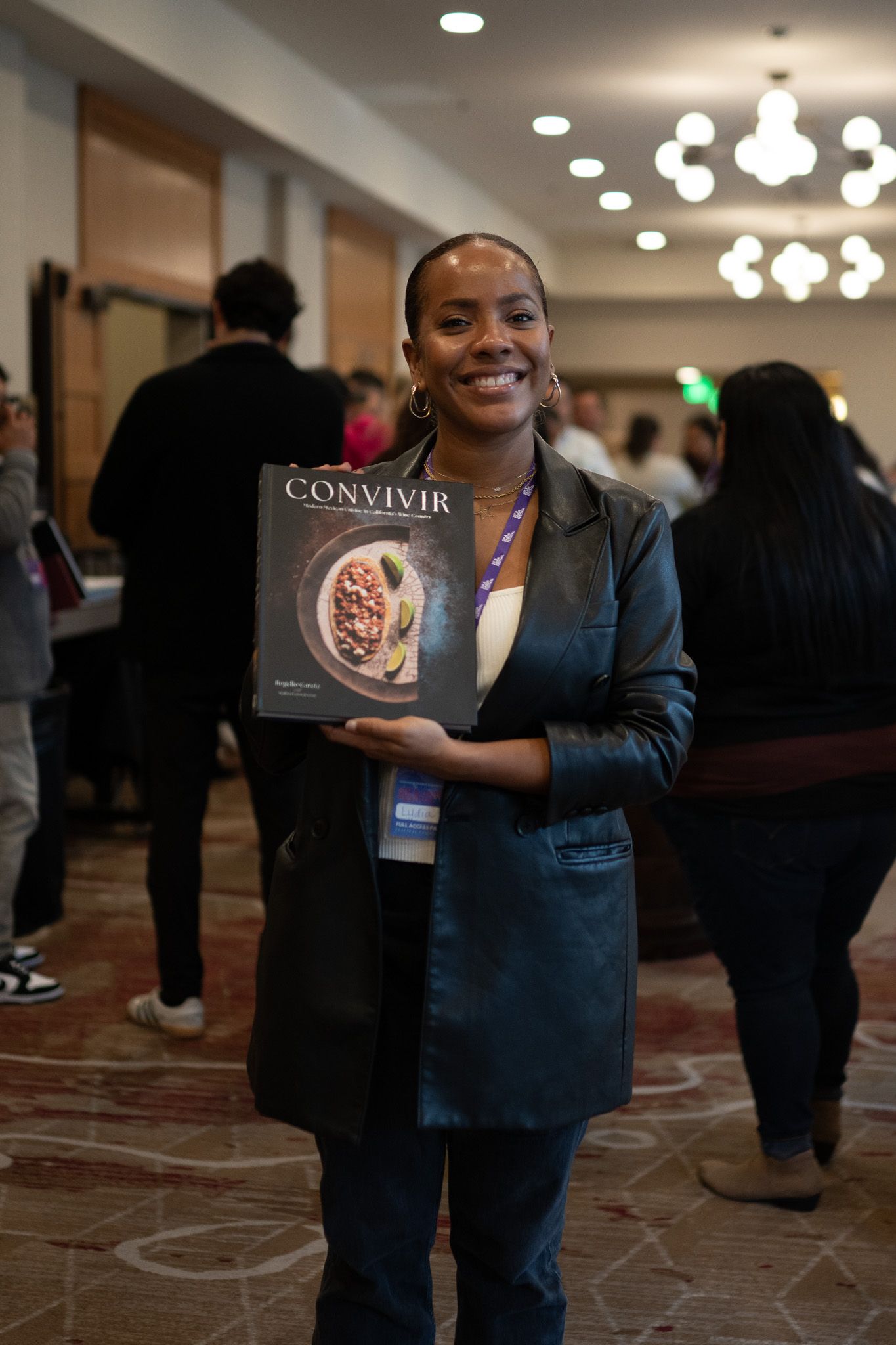 Person holds a cookbook titled 'Convivio' while standing in an elegant room with chandeliers.
