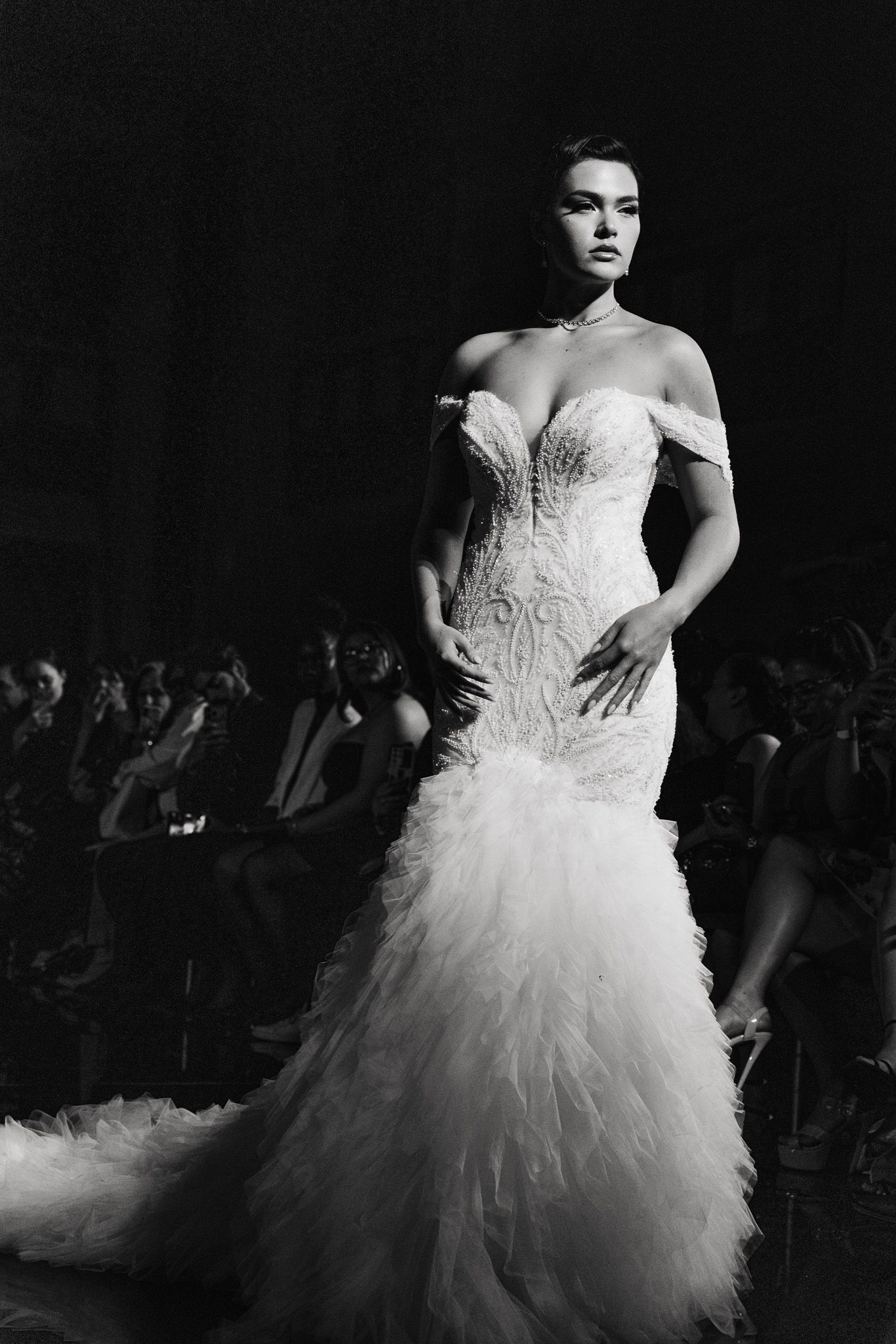 A model walks the runway in a dramatic white strapless wedding gown with ruffled tulle skirt during a fashion show.