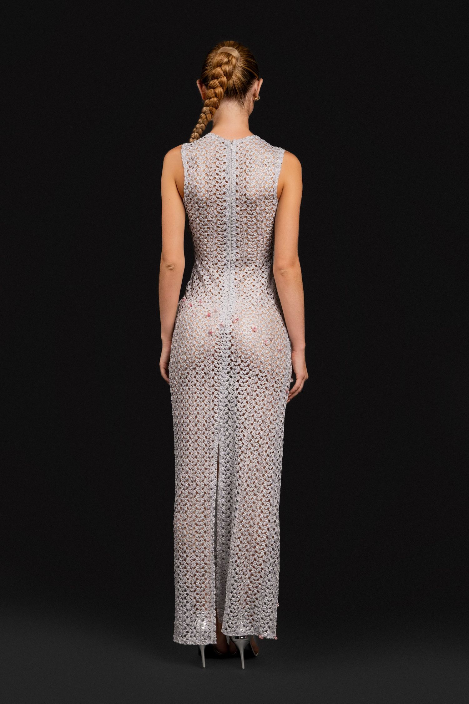 Back view of woman in sleeveless white crochet lace maxi dress with center slit and braided hair.