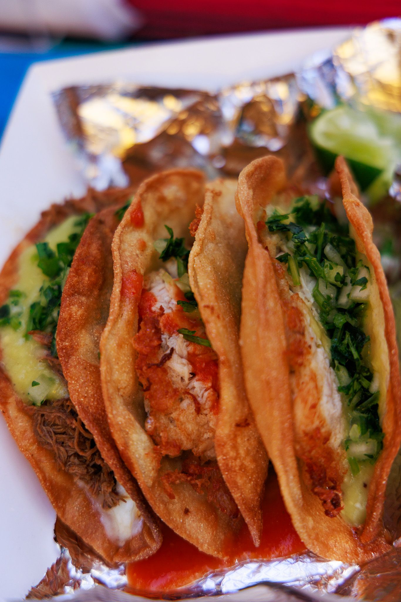 Three crispy street tacos topped with fresh cilantro, salsa, and avocado served on foil-lined plate.