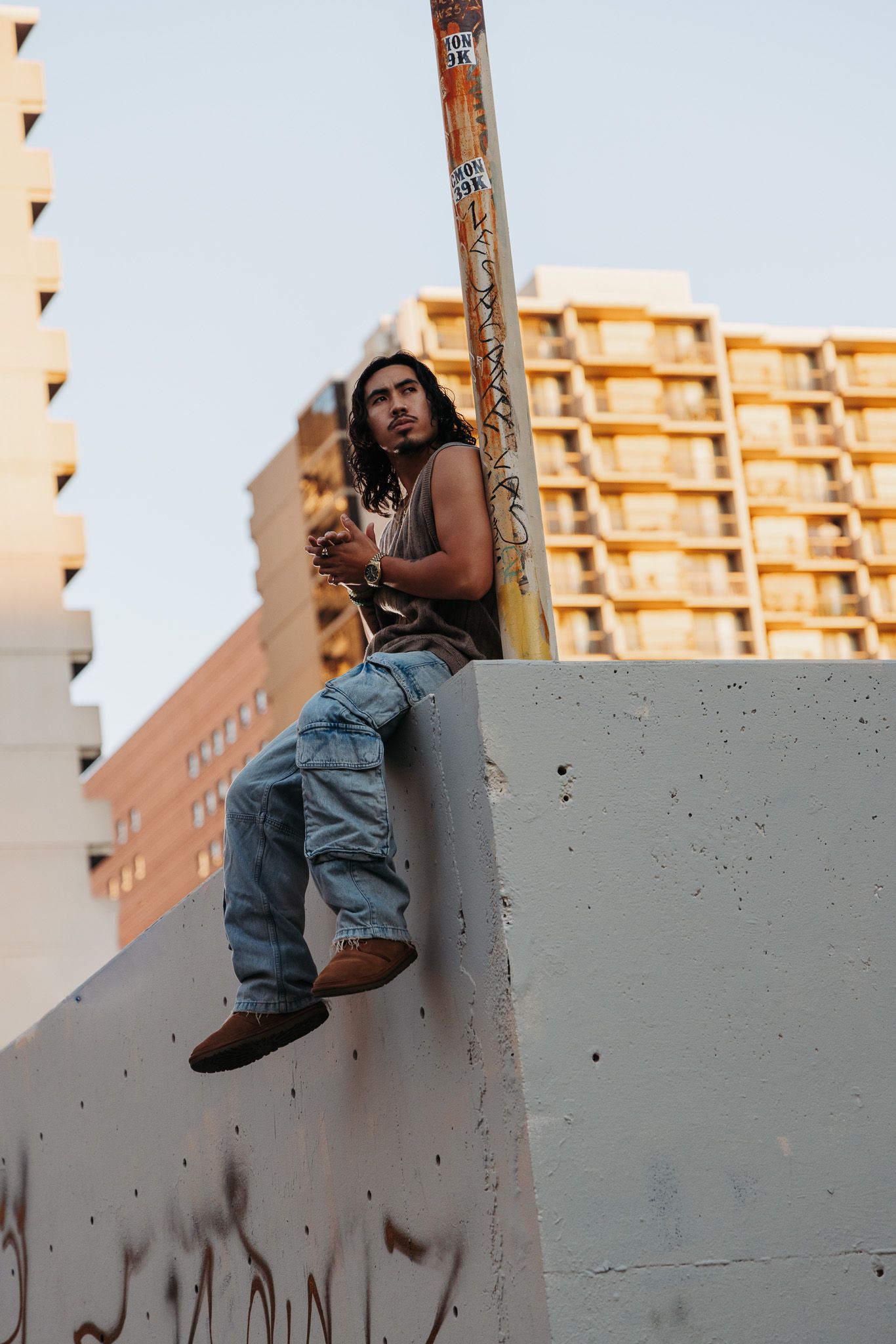 A sequence of photos showing someone in denim overalls sitting and posing against a concrete wall at sunset.