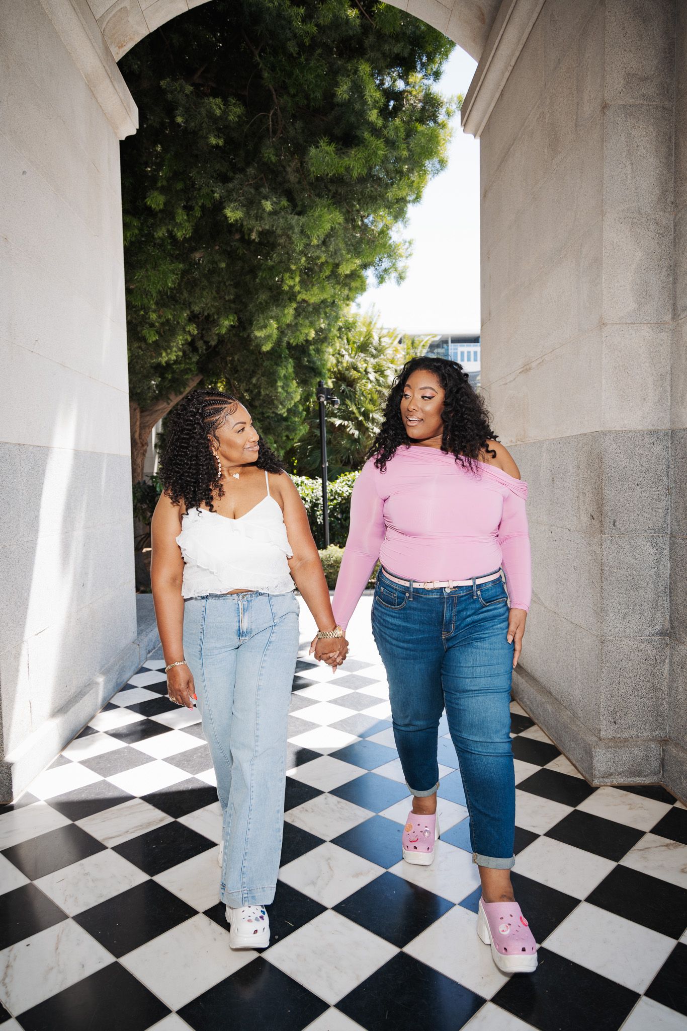 Two people wearing jeans stand on a black and white checkered floor in an outdoor covered walkway.
