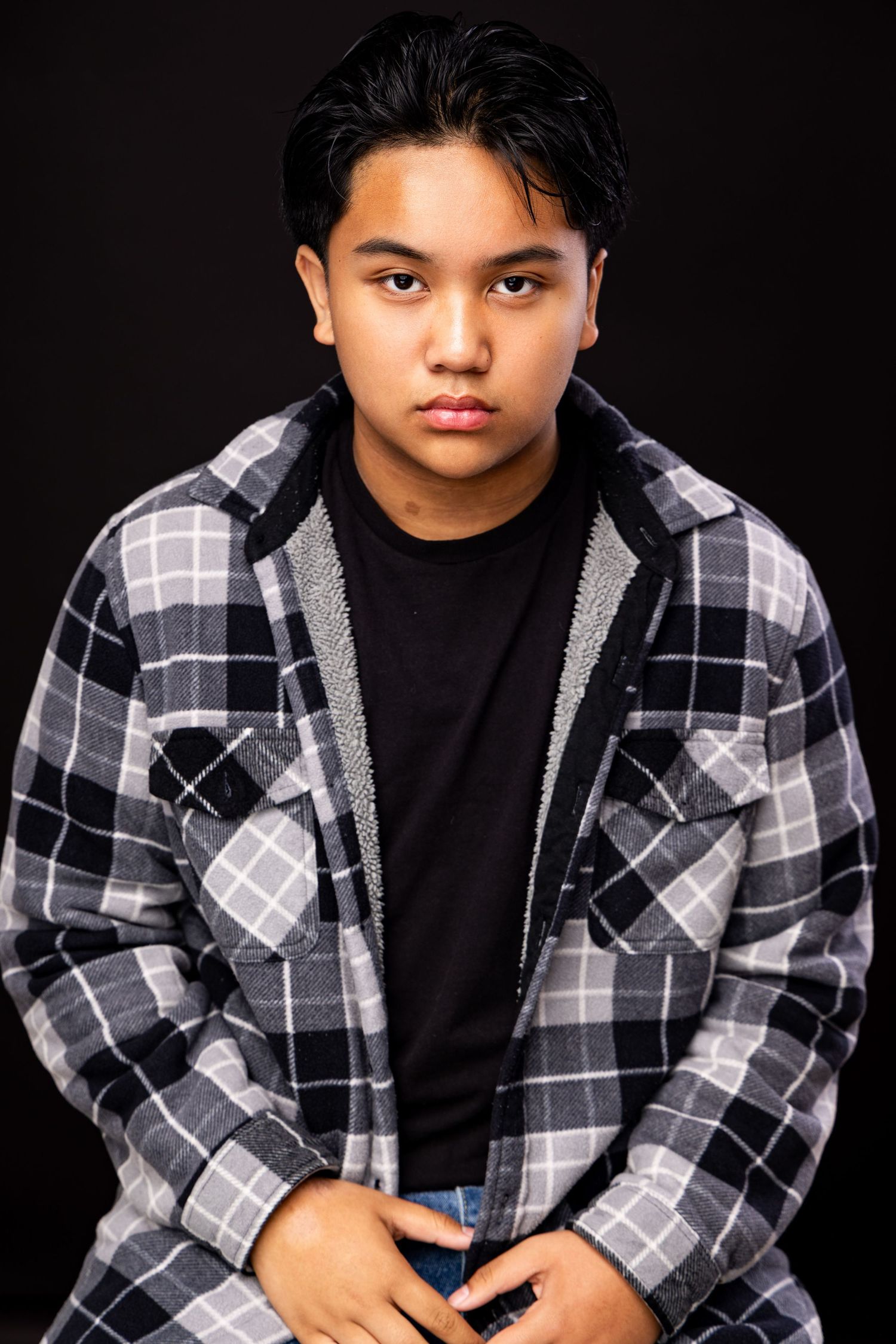 Studio portrait photoshoot showing four similar poses against a black background wearing a plaid jacket and black shirt.