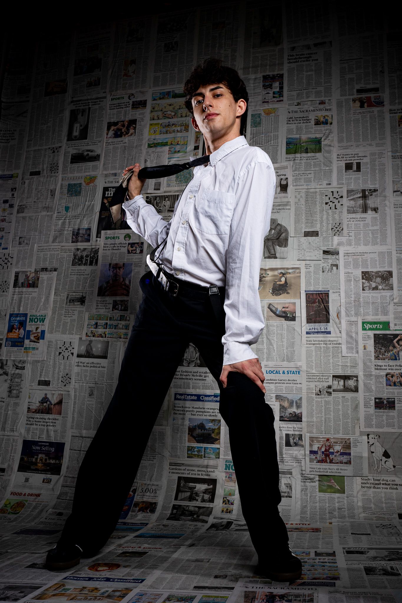 A performer poses in front of a newspaper wall showing different dance poses in black and white.