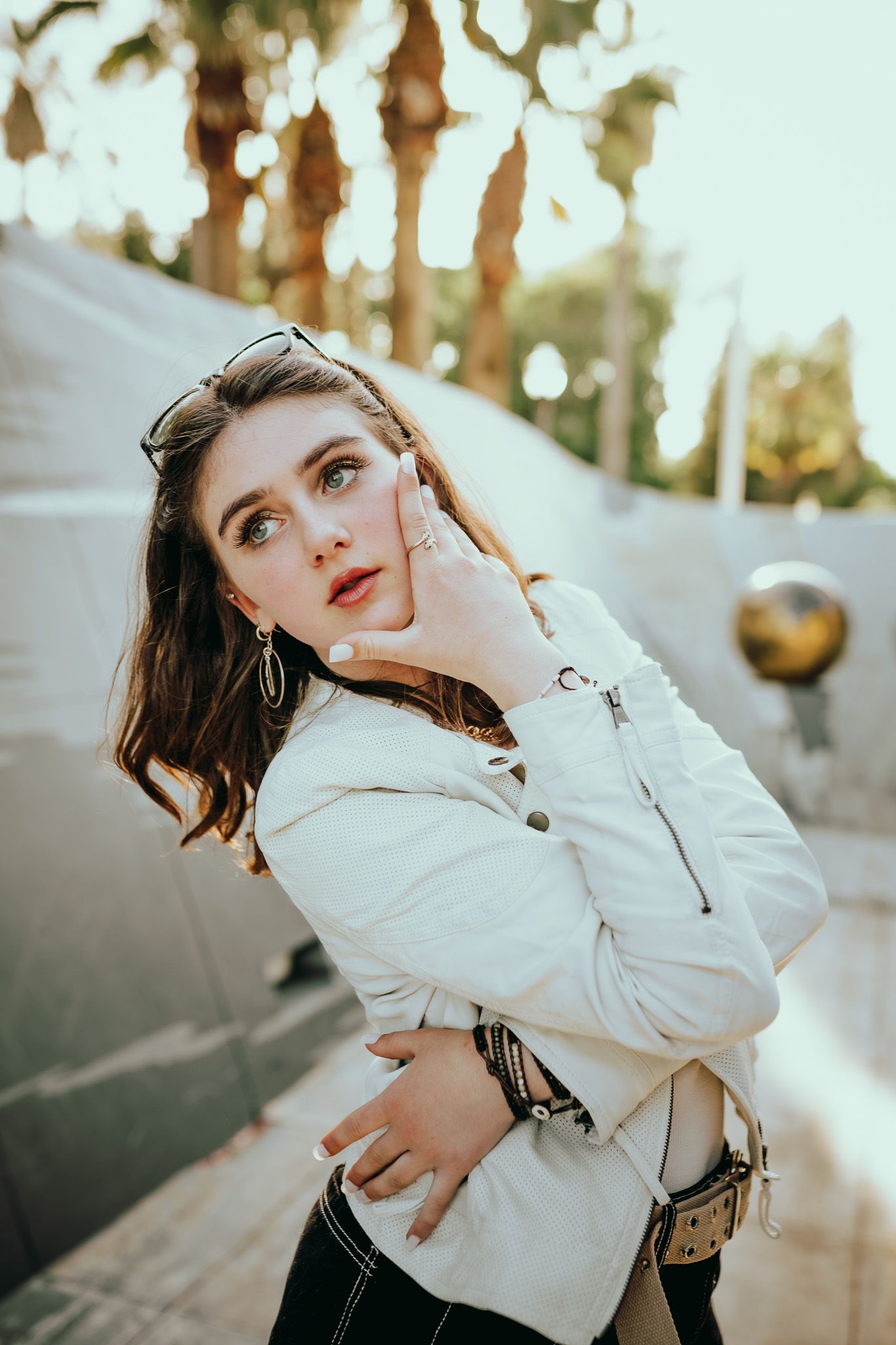 Artistic outdoor portrait in warm lighting with white jacket against blurred natural background and bokeh effect.