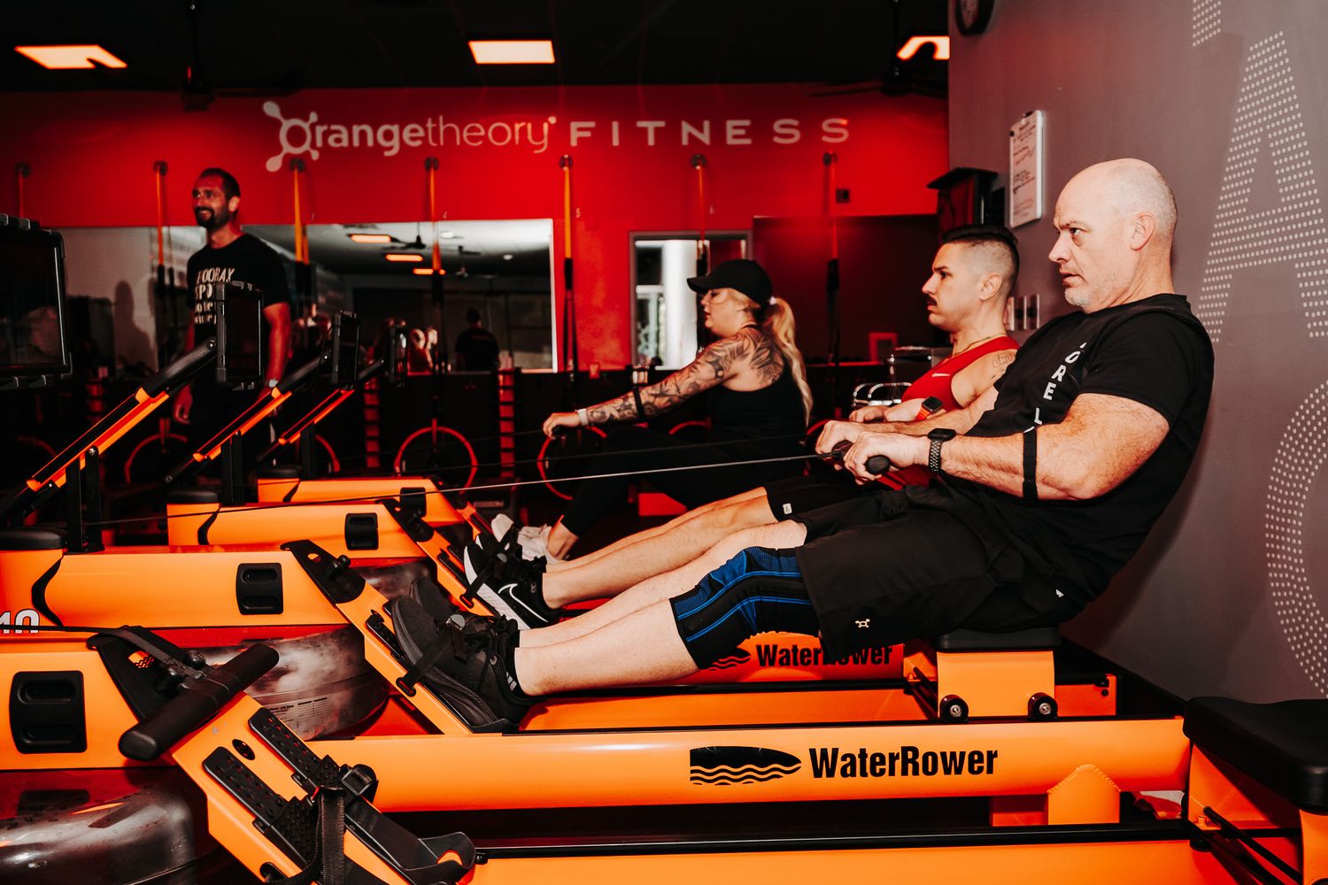 A row of orange fitness equipment in a red-lit gym studio designed for Orangetheory workouts and training.