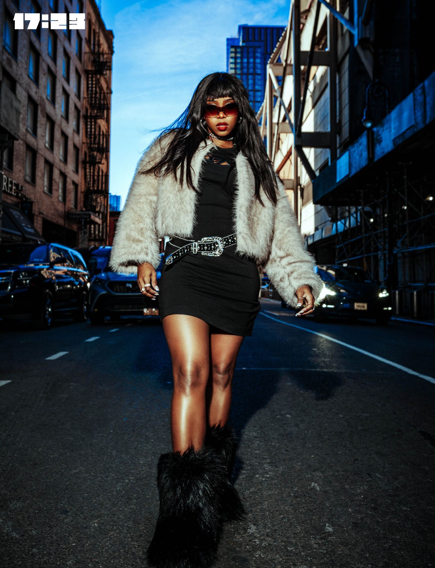 Street style shot of model wearing fluffy white coat and black dress walking in urban setting.