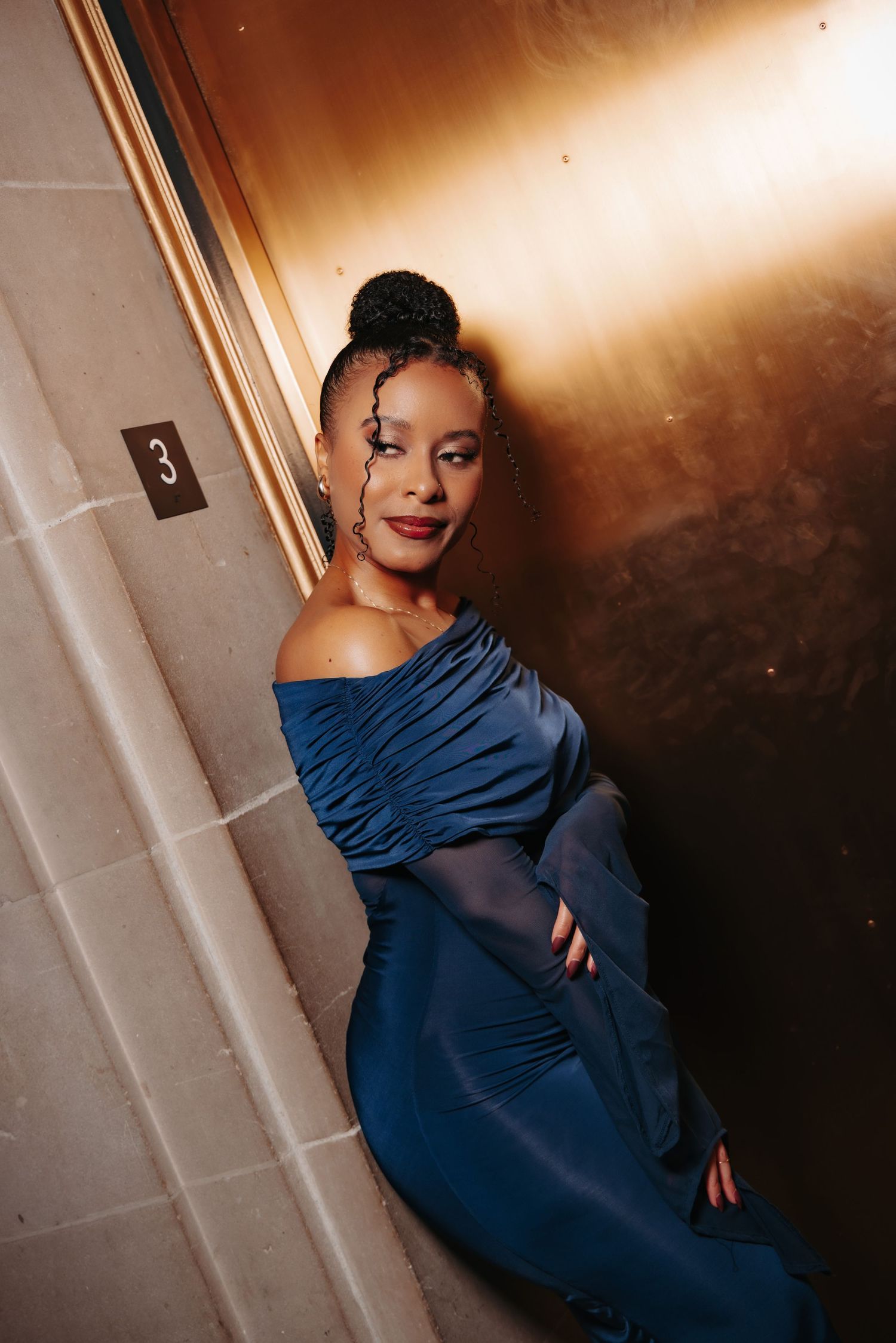 Portrait series in dimly lit space shows person wearing a striking navy blue gown against dramatic shadowy background.