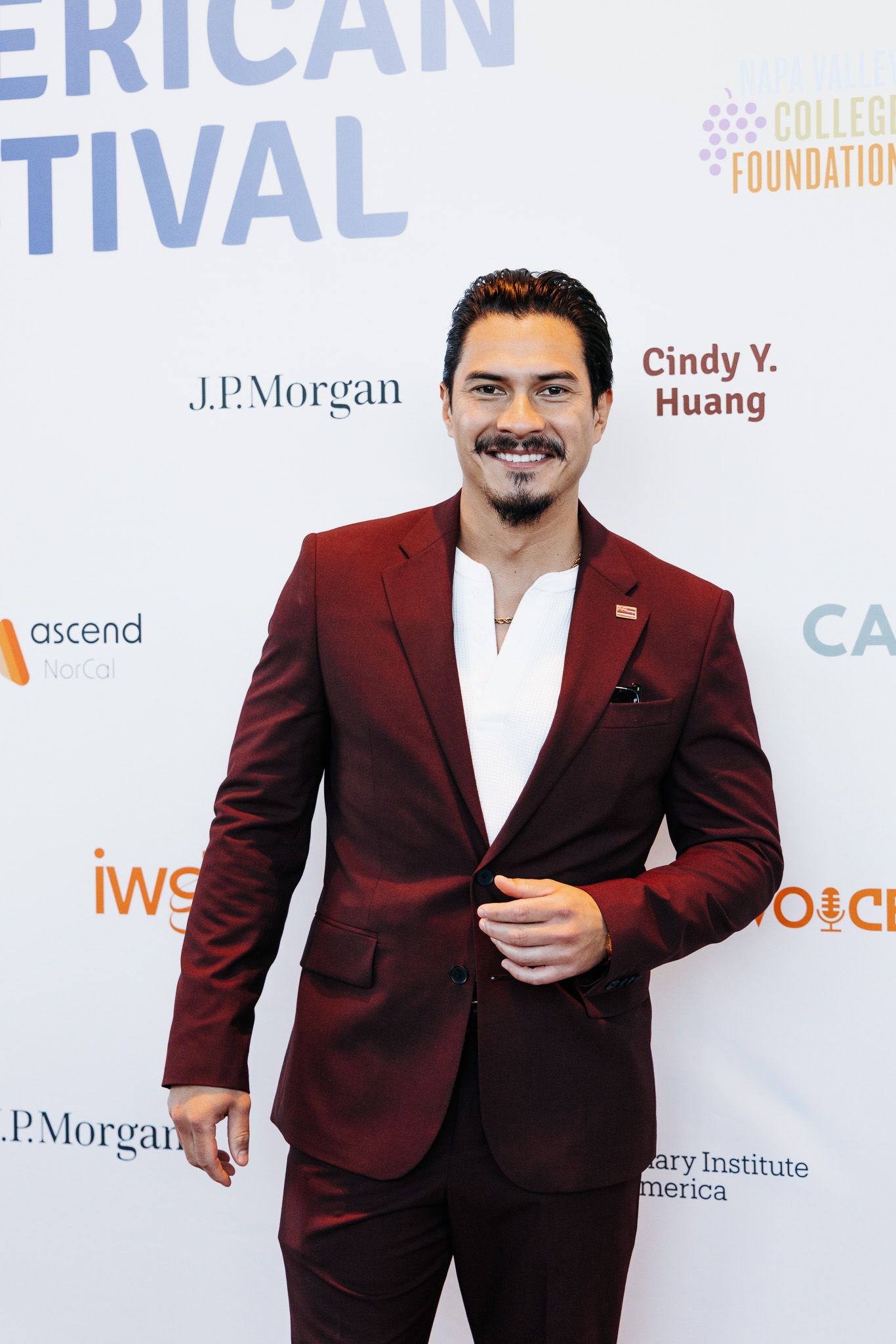Man in burgundy suit smiling at American Film Festival red carpet event with J.P. Morgan sponsors.