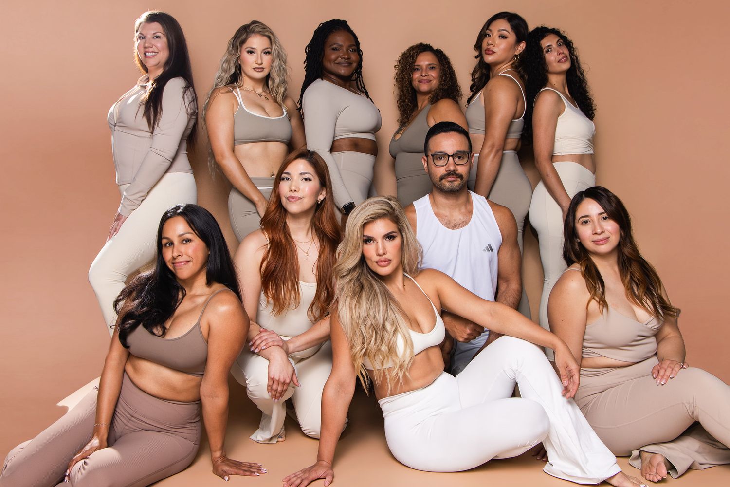 Diverse group of fitness instructors in neutral activewear posing together in beige studio.