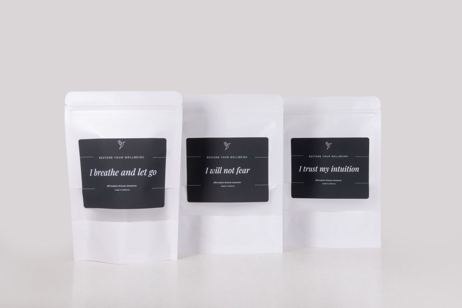 Three white tea pouches with black labels reading i breathe and let go, i will not fear, and i trust my intuition.