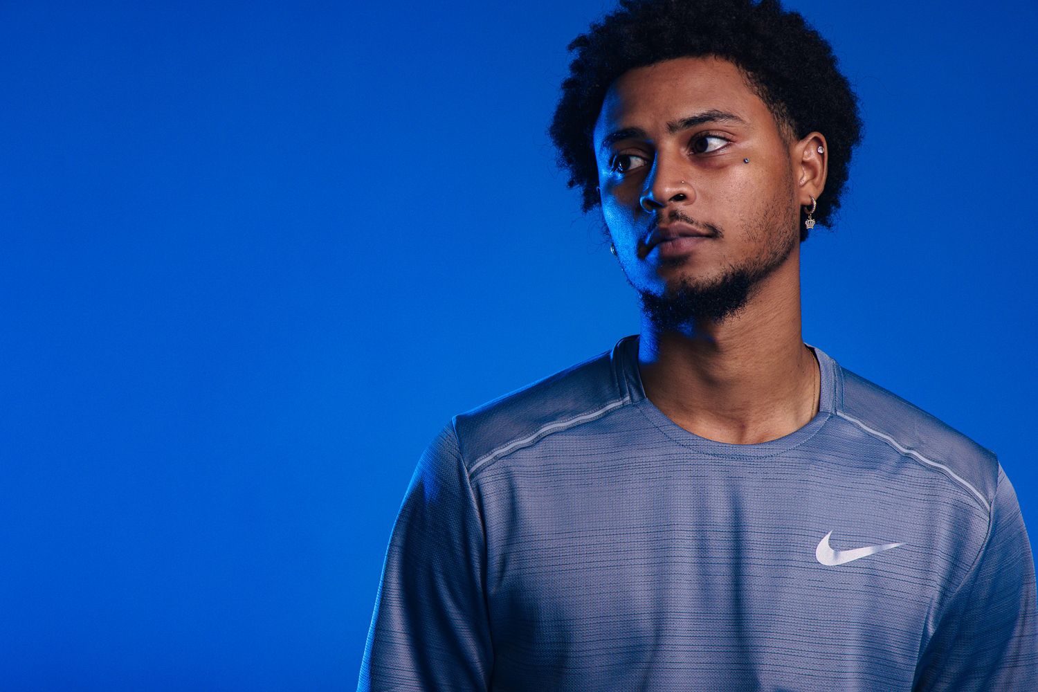Young man wearing a gray Nike athletic shirt posing against a vibrant blue background.