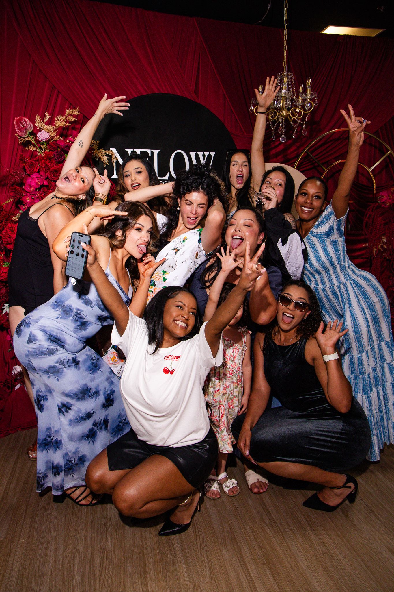 A group celebrating at NFLOW studio with red curtain backdrop and floral decorations.