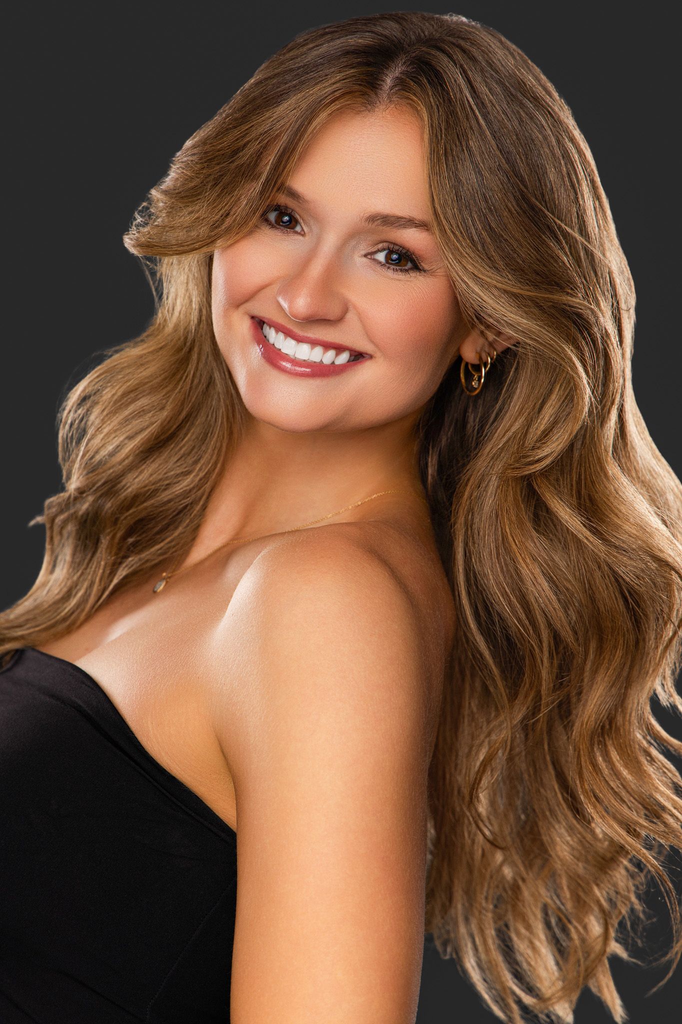 Professional beauty portrait with wavy blonde hair and bright smile against dark background.