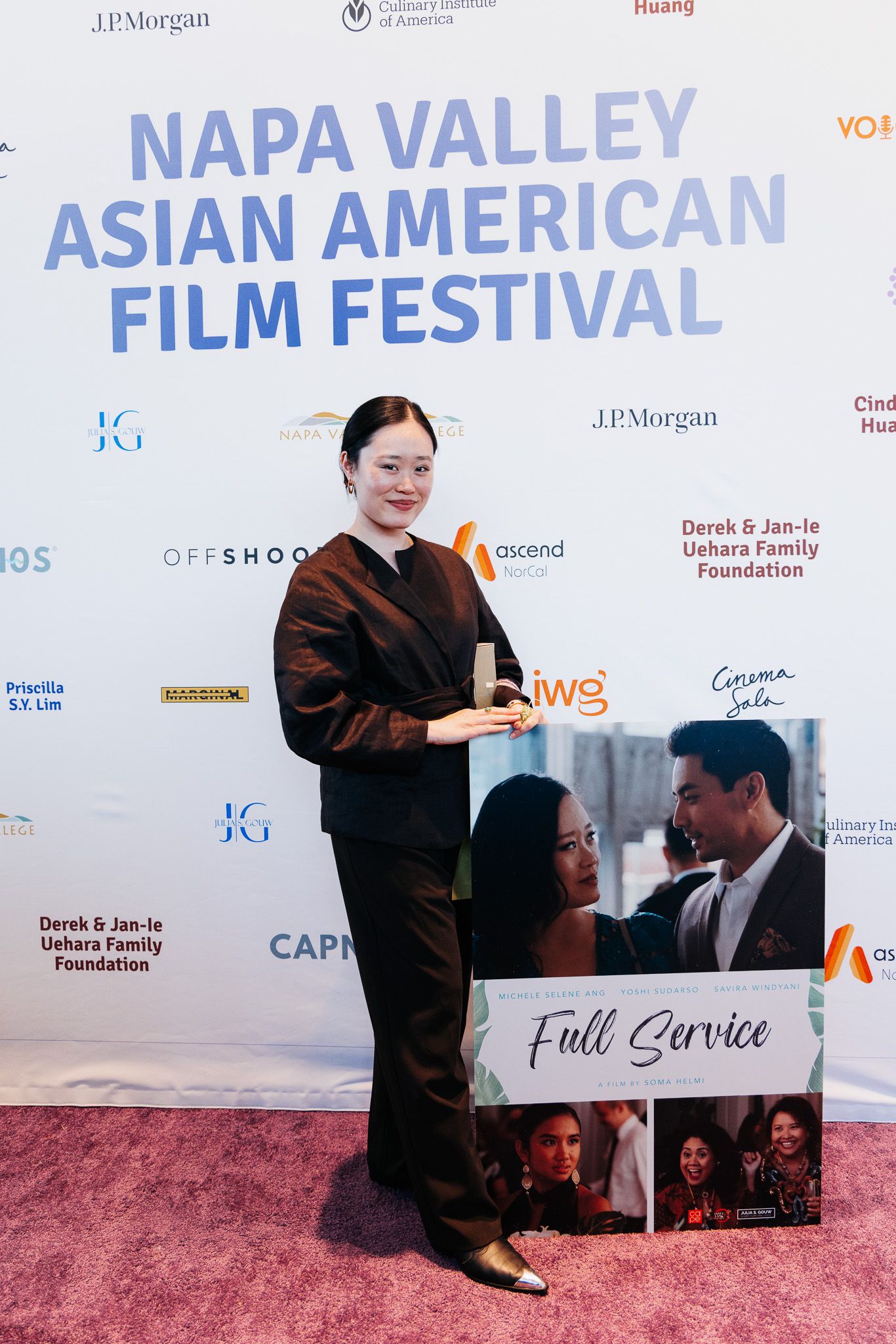 A person in dark clothing poses with a movie poster at a film festival.