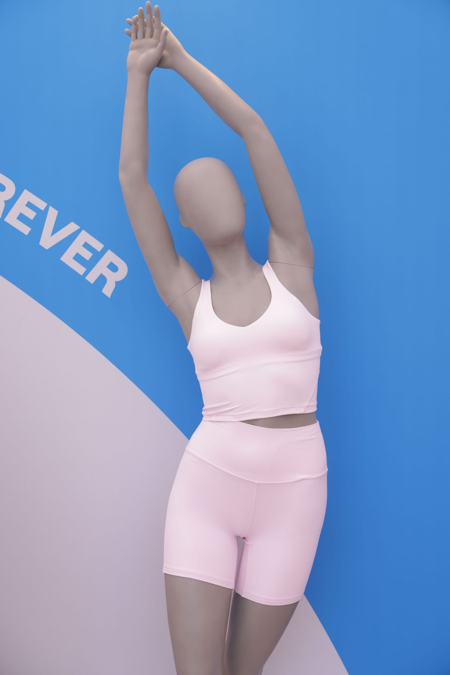 Athletic figure in pink workout attire stretching against blue and white backdrop.