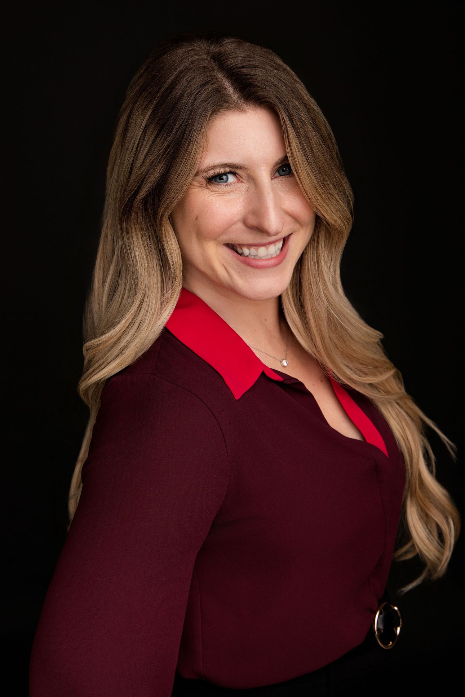Professional studio portrait against black background featuring burgundy top and blonde hair with warm lighting.