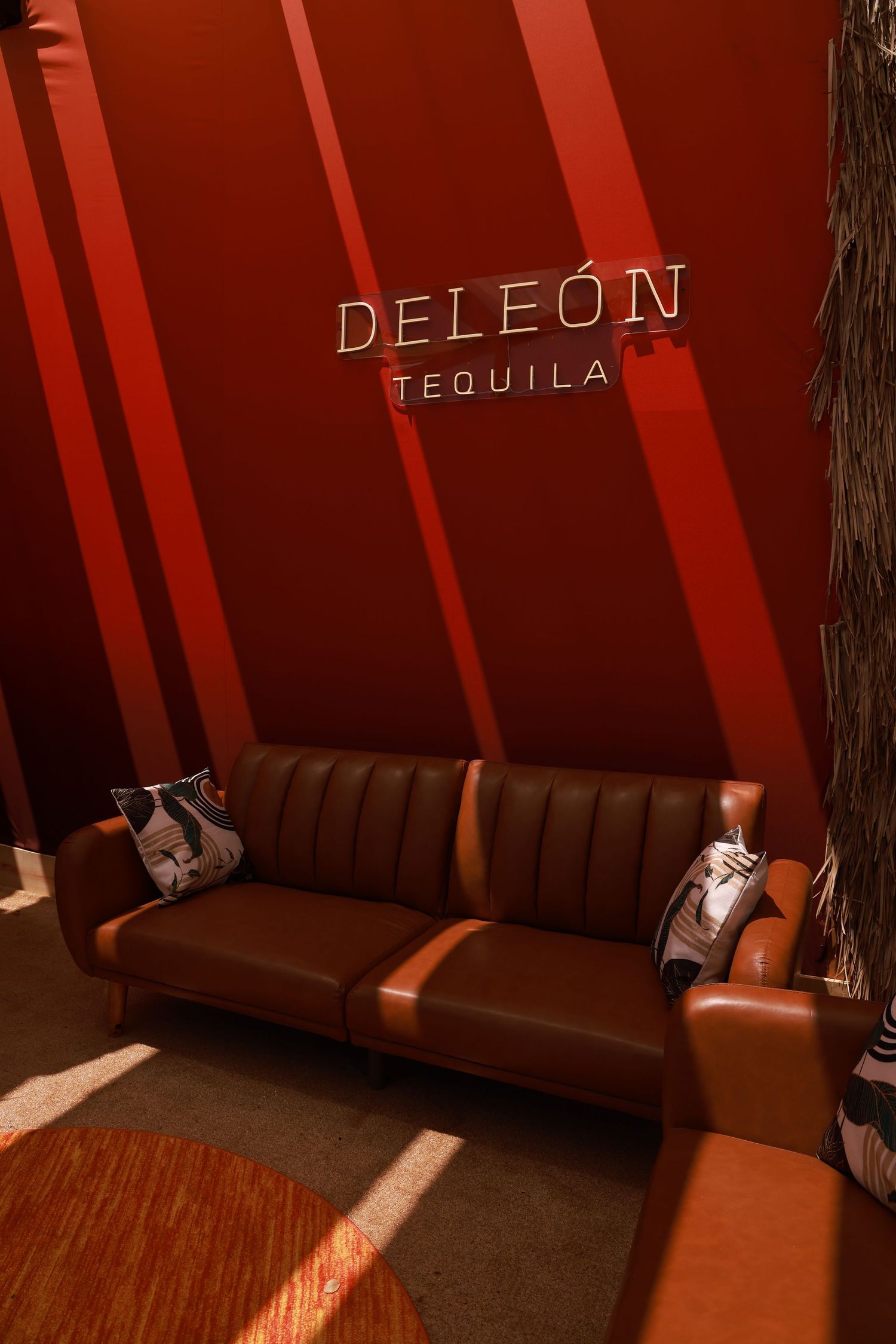 Brown leather banquette seating illuminated by angled light beams with DeLeon Tequila signage on display.