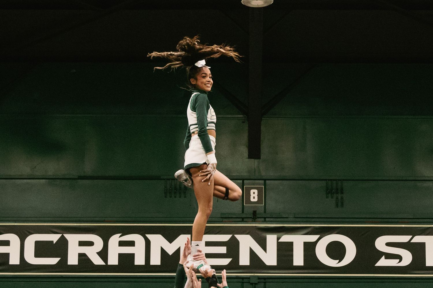 Sacramento State cheerleader jumps mid-air in front of Sacramento State sign.