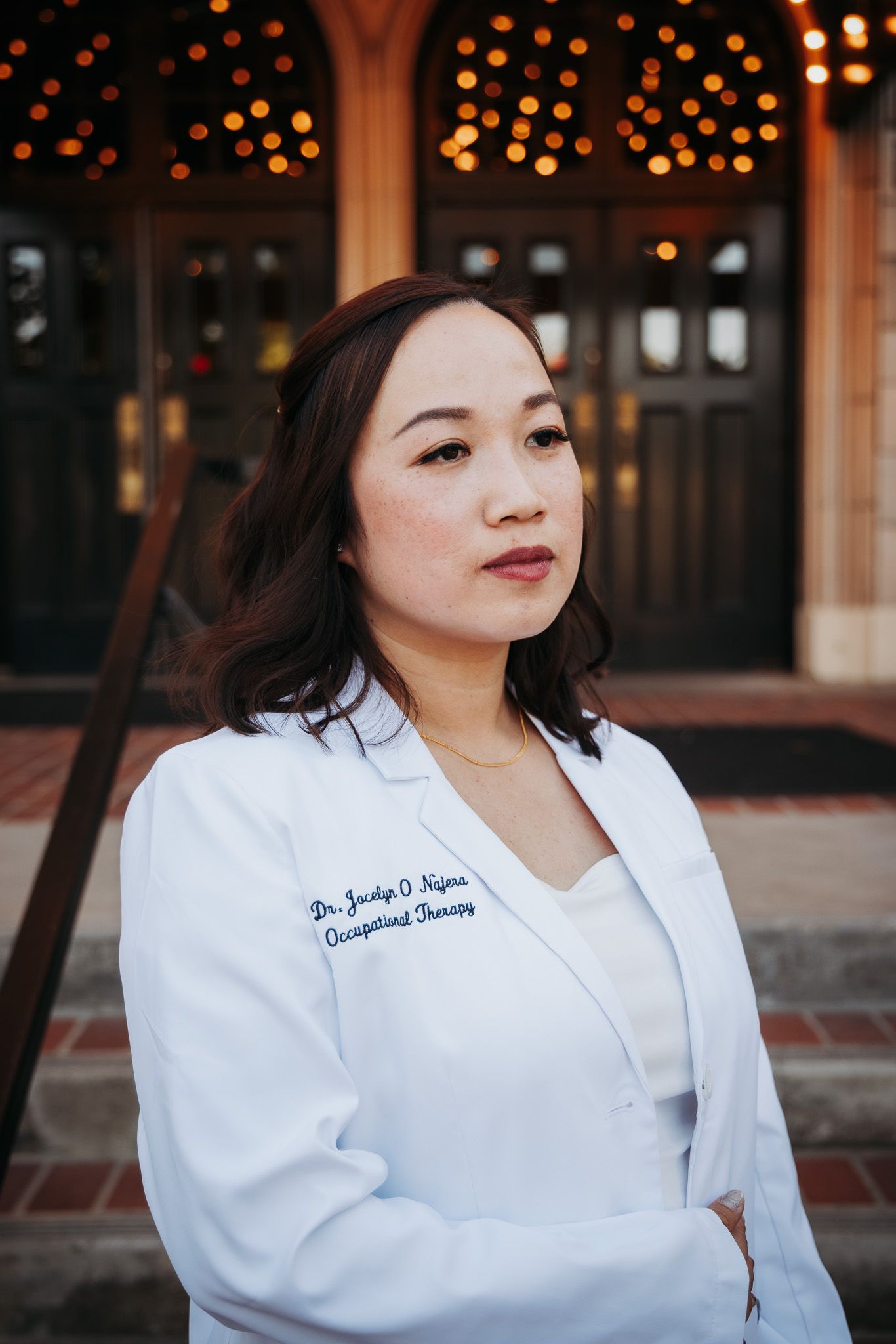 Person wearing a white medical coat looking sideways in front of bokeh lights background.