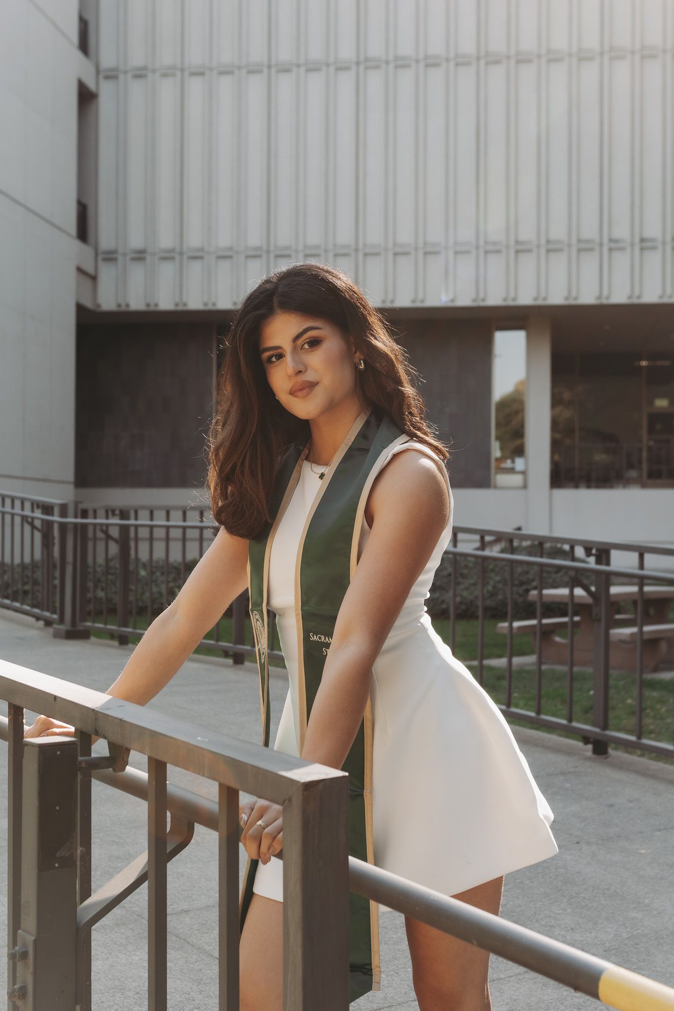 A person in a white outfit poses on a metal railing outside a building with vertical lines in the background.