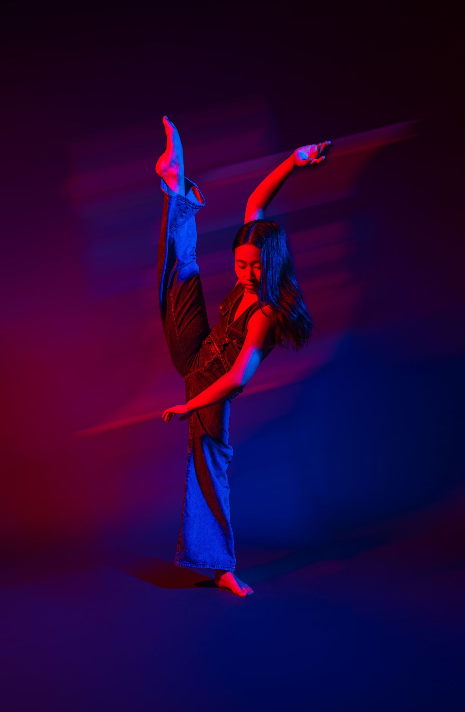 Contemporary dancer leaping through air illuminated by dramatic red and blue stage lighting effects.