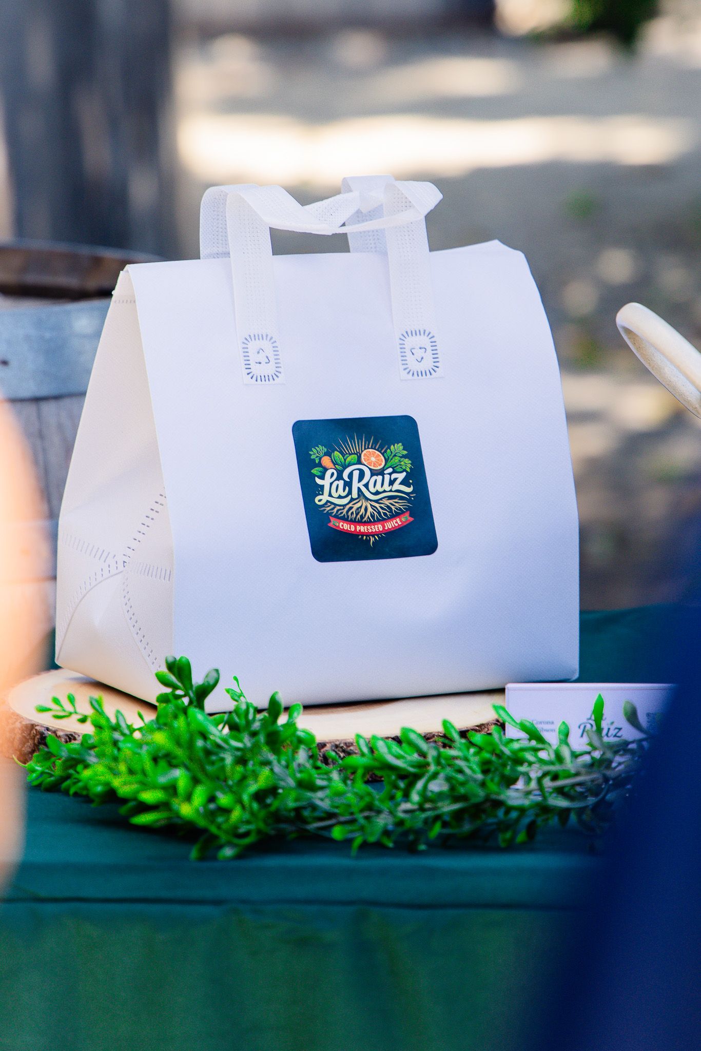 White La Ruiz branded gift bag with logo sticker displayed outdoors near green plants.