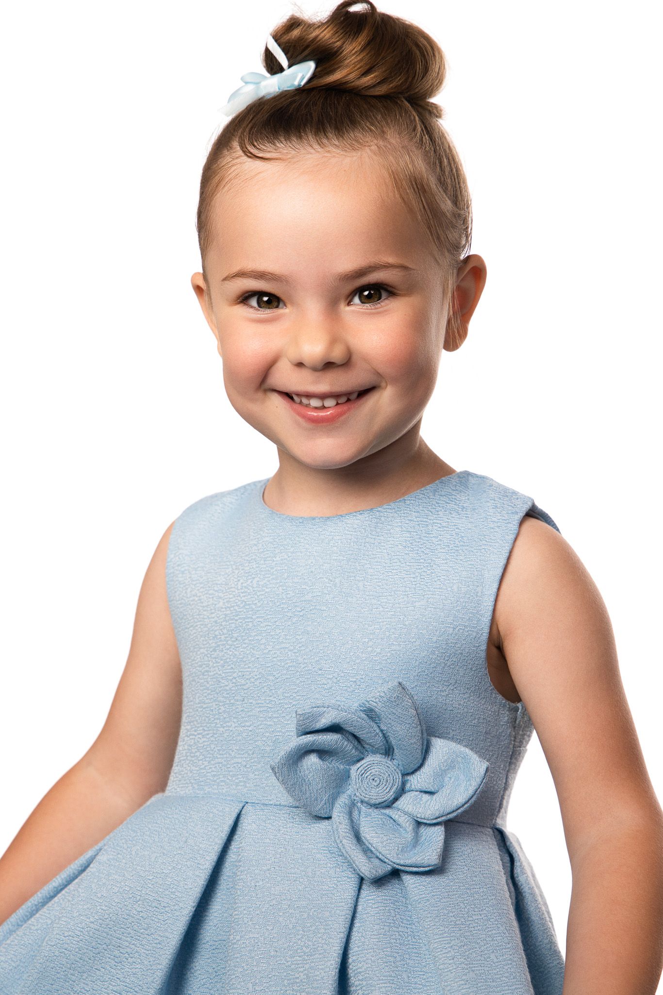 Small child wearing light blue dress with bow detail smiling at camera.