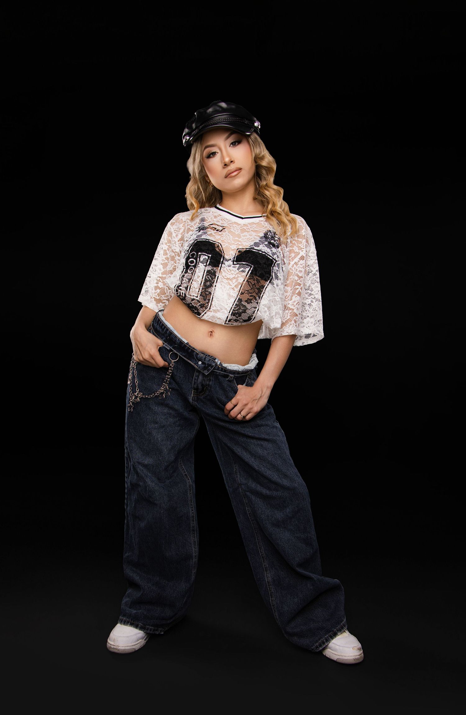 A person in baggy denim overalls and a cropped floral top poses against a black background in various dance-like stances.