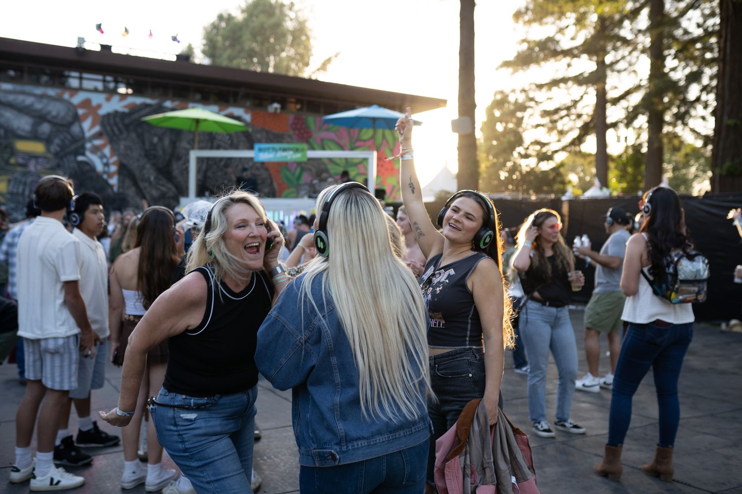 Crowd of attendees mingling at an outdoor evening festival with tents and trees in background.
