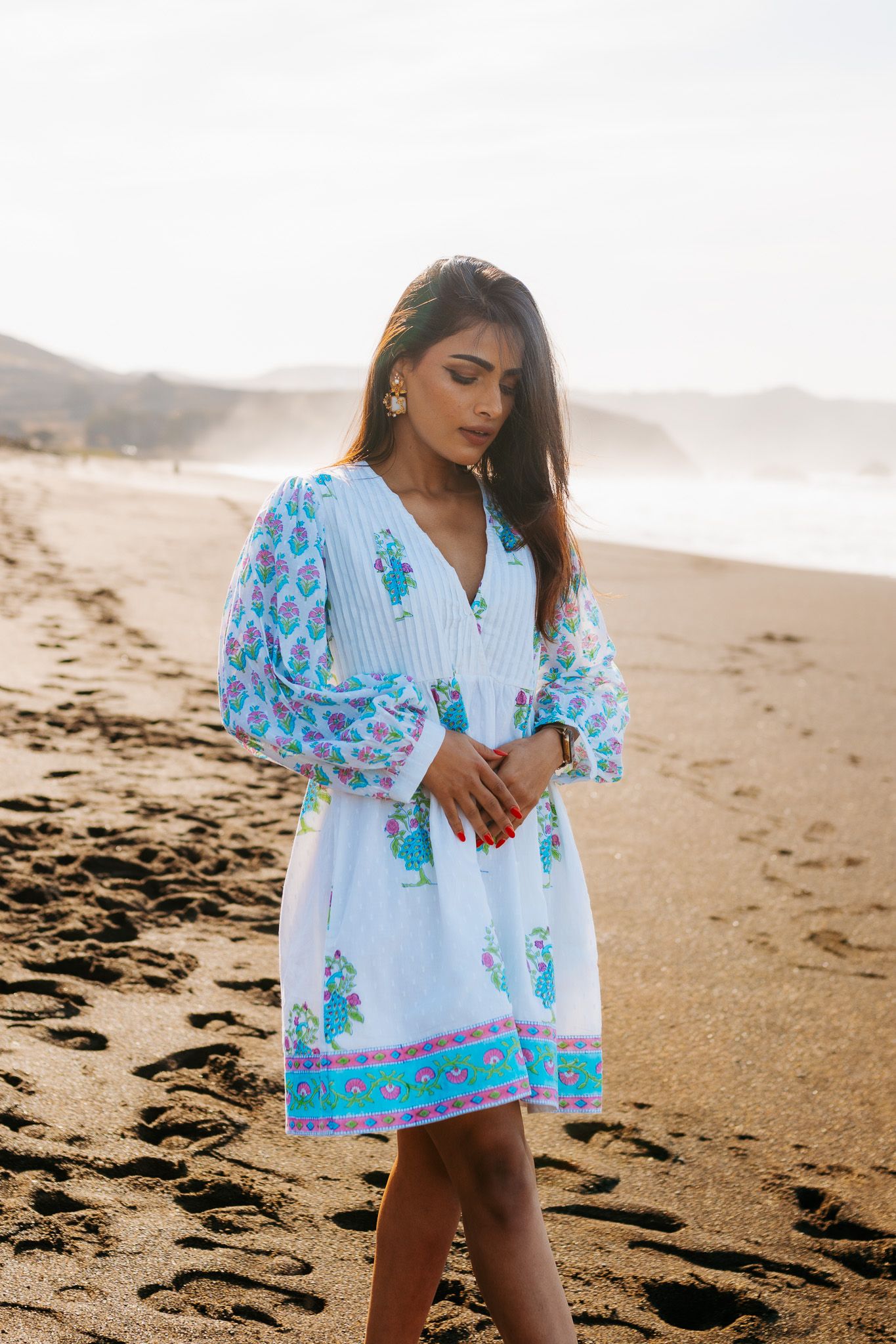 A white and turquoise floral dress with balloon sleeves worn on a serene beach during golden hour.