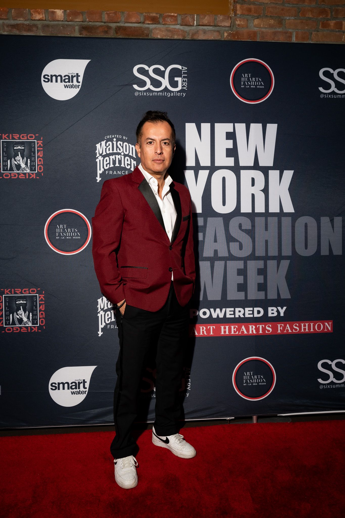 Attendee in burgundy blazer and black pants poses at New York Fashion Week event on red carpet.