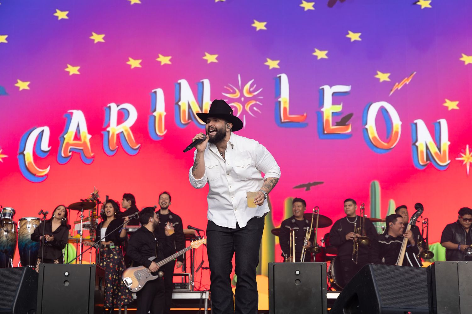 A performer on stage with a colorful backdrop featuring the text 'CARIN LEON' and star decorations.