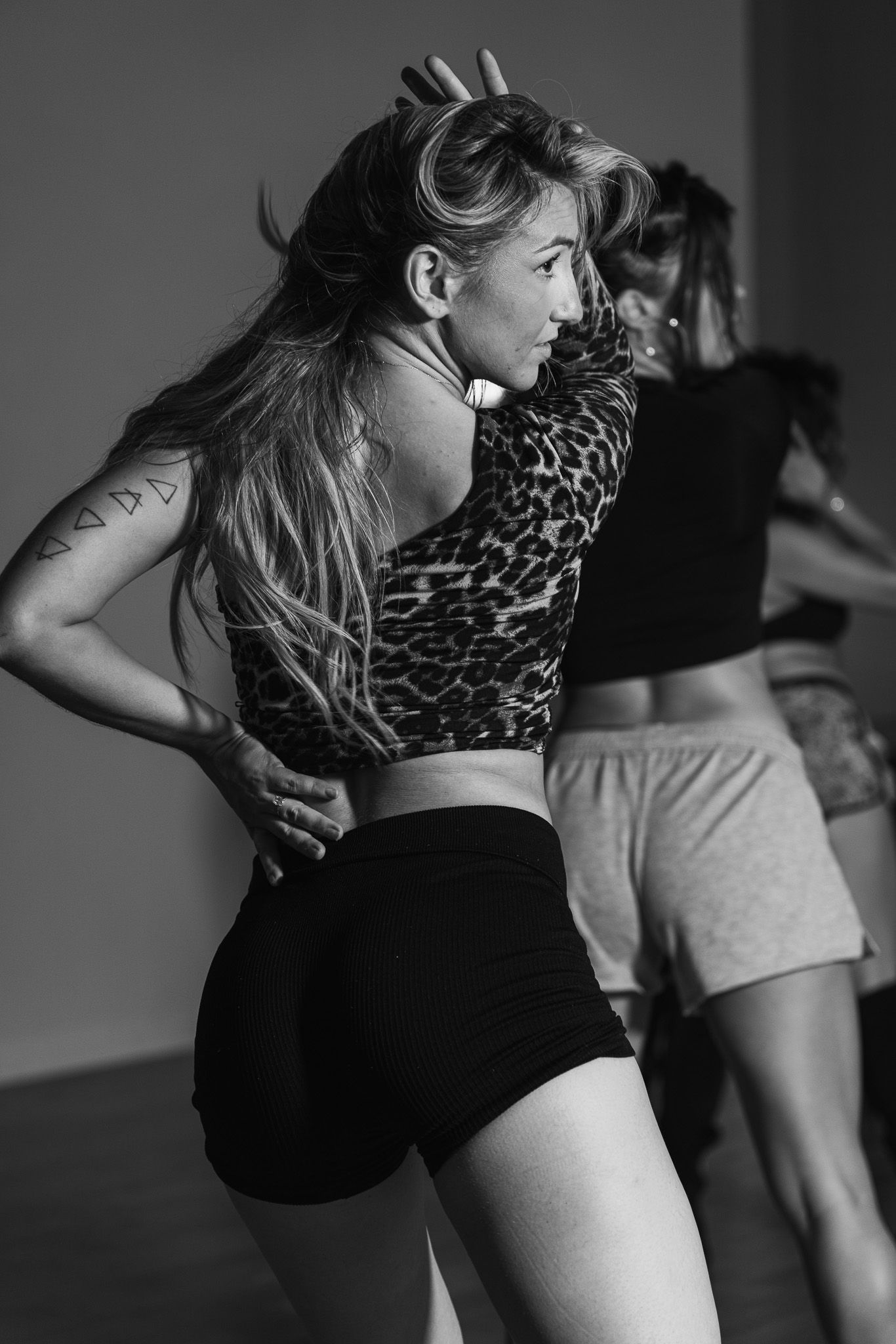 Black and white photo of women dancing in a studio, wearing crop tops and shorts, with dynamic poses and flowing hair.