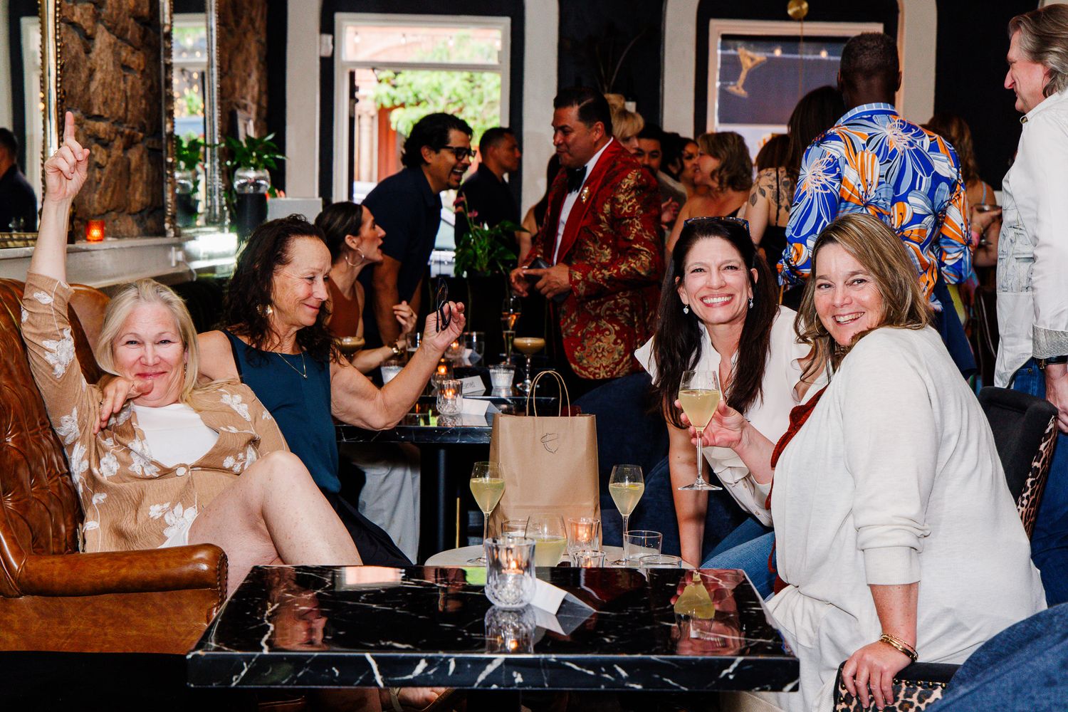 Four women smile and pose with wine glasses at an elegant indoor social gathering event.