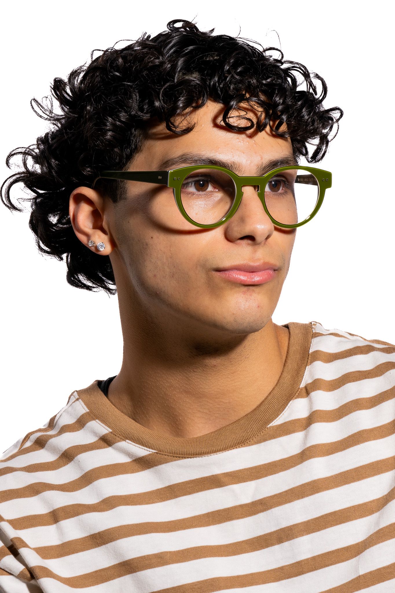Young man with curly black hair wearing green glasses and a striped beige shirt, studio portrait.