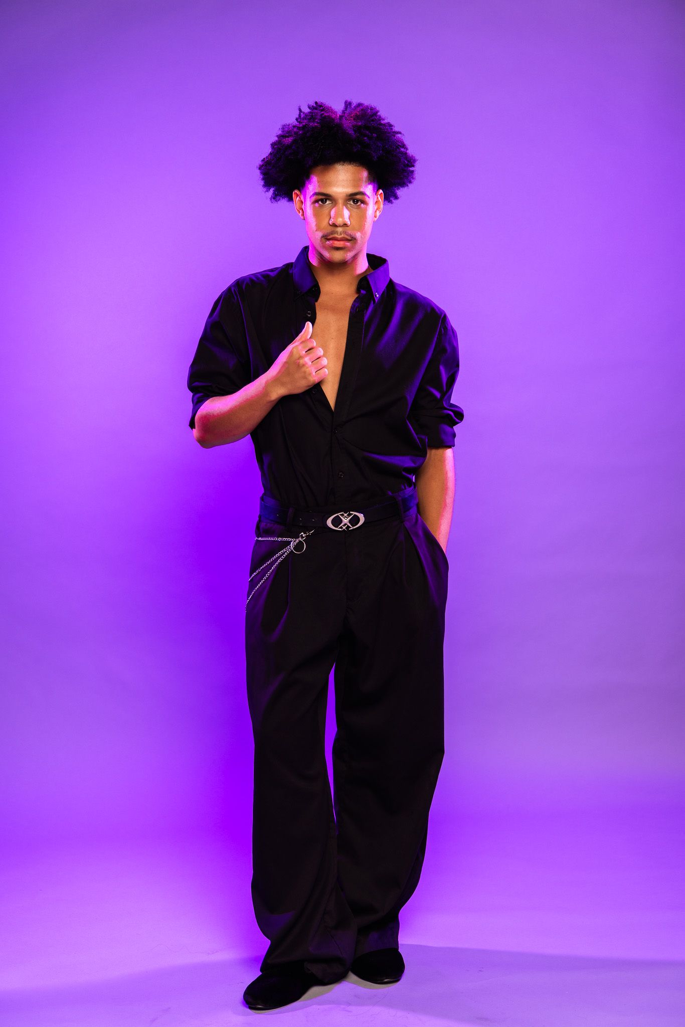 A figure poses in a black outfit against a vibrant purple studio backdrop in a fashion photography series.