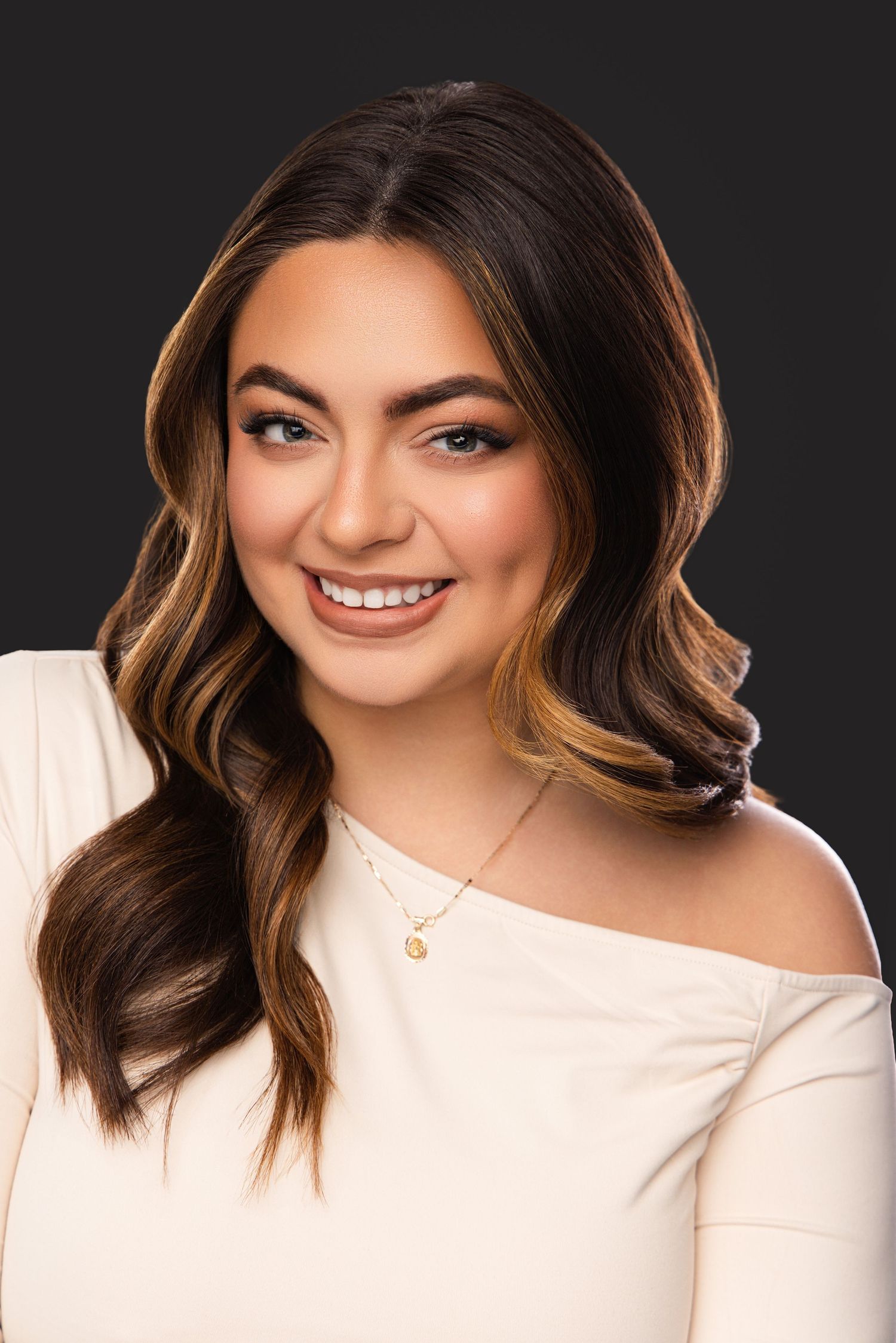 Professional headshot portrait of someone wearing a white top against a dark background with warm lighting.