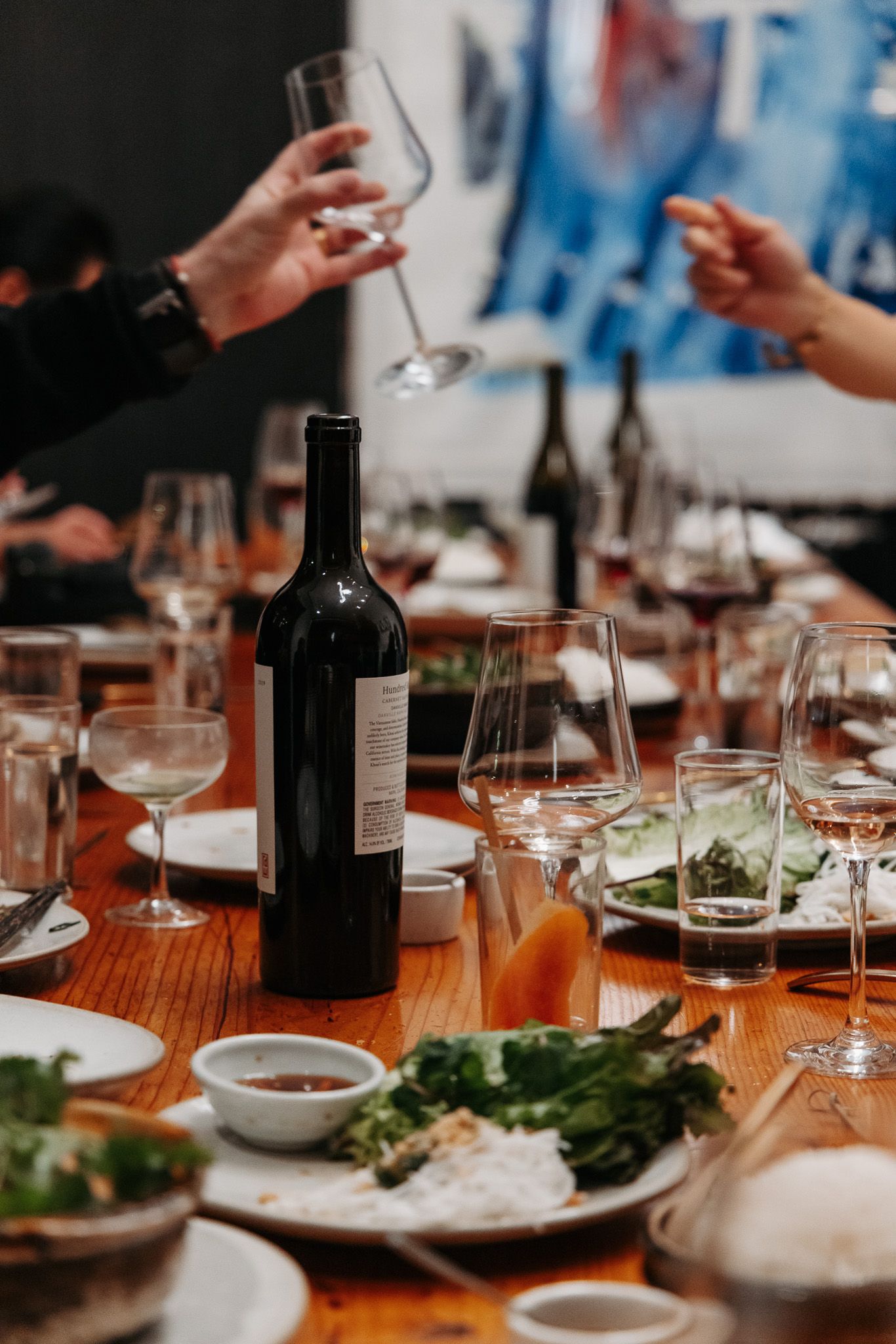 Elegant dinner table setting with wine glasses, plates and shared dishes in dim lighting.