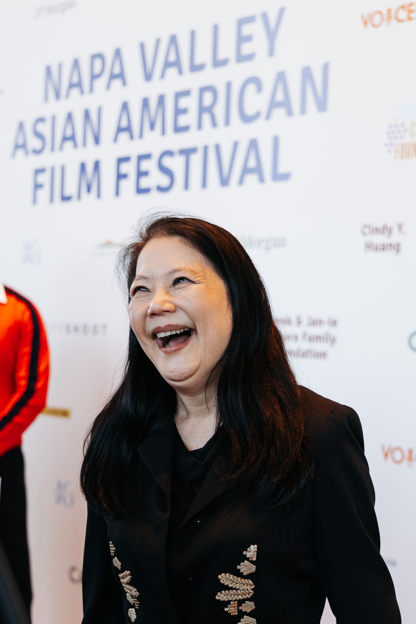 A person in black attire laughs expressively in front of a film festival backdrop.