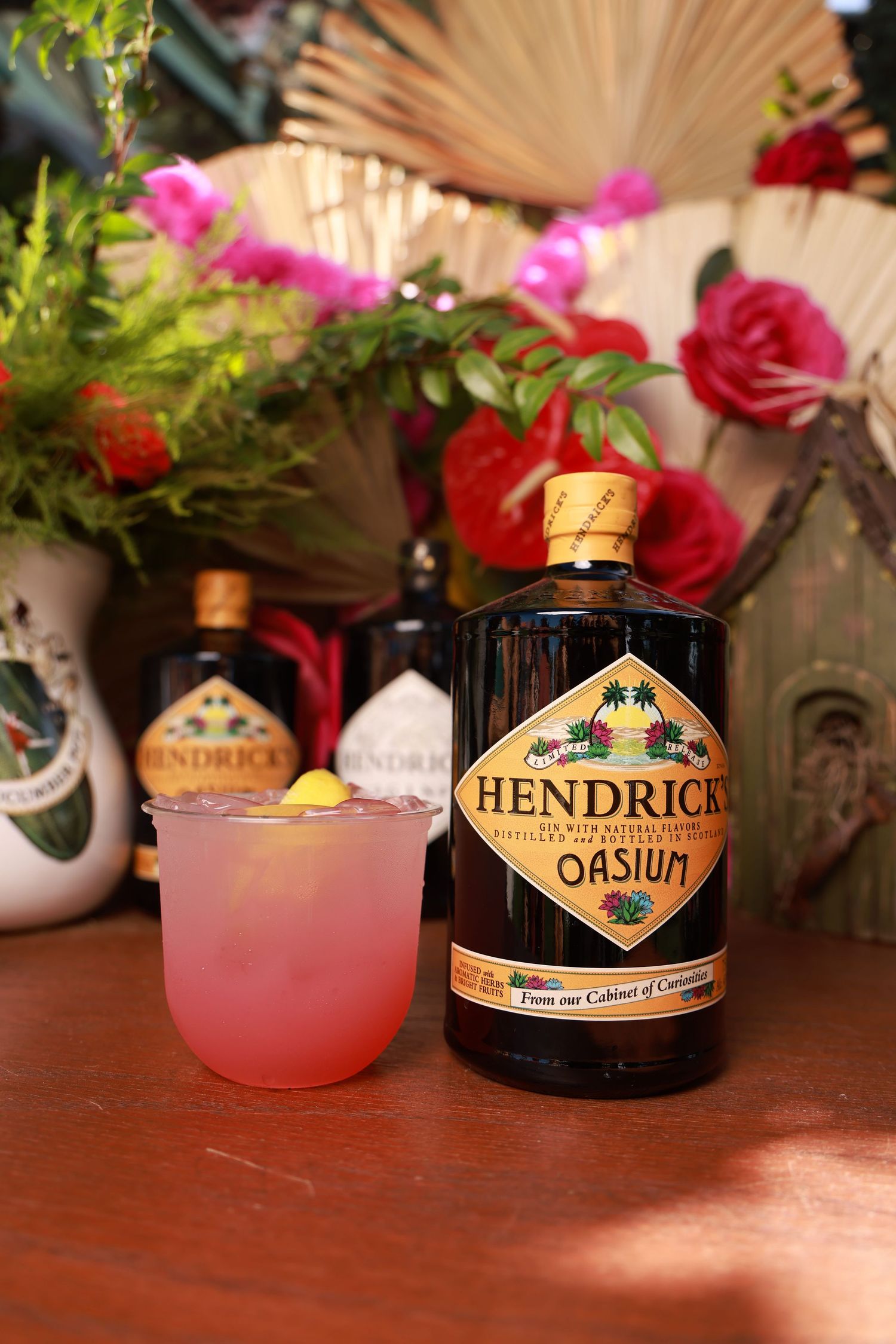 Hendrick's gin bottle and pink cocktail displayed with roses and decorative elements on wooden surface.