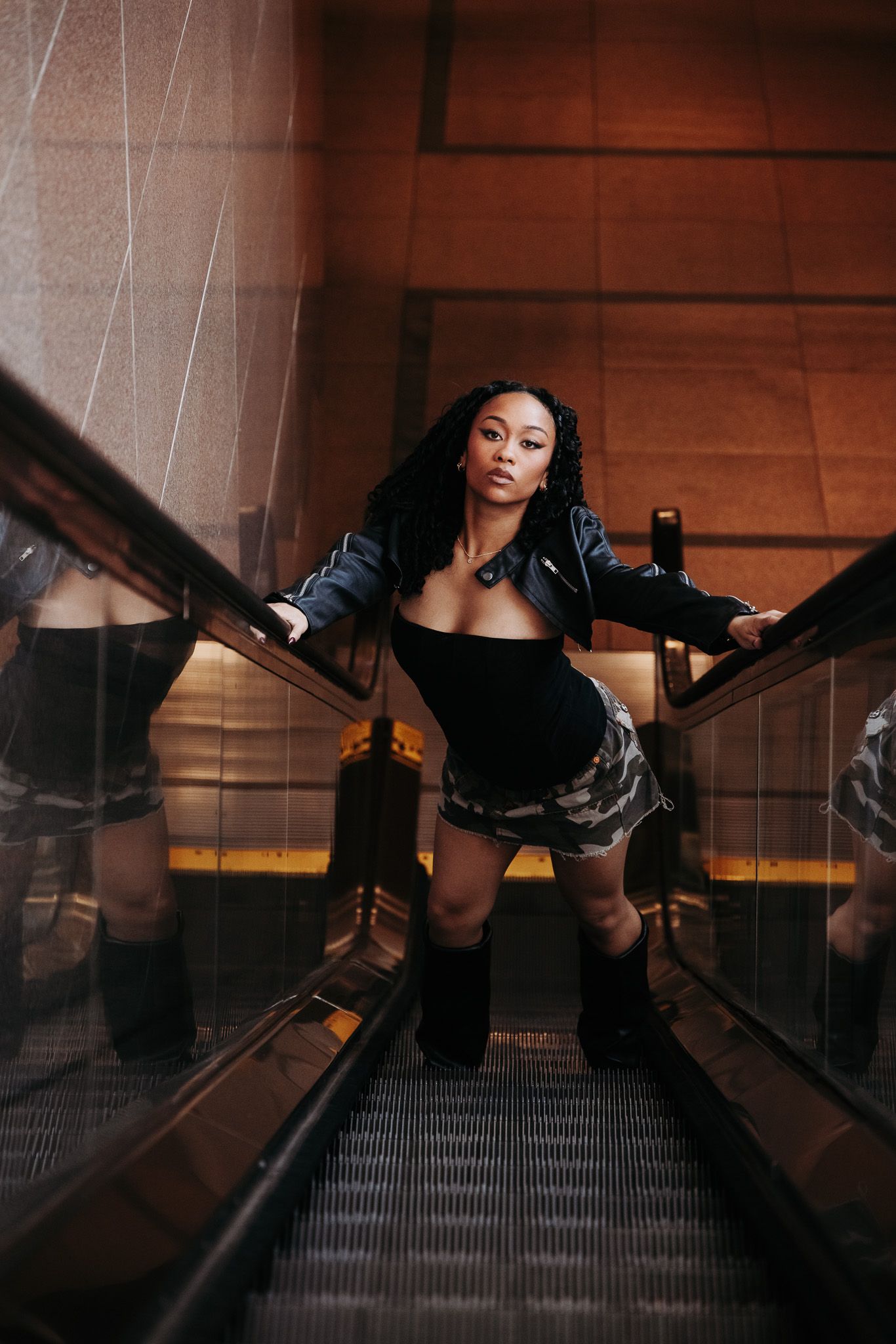 A person in black clothing poses dramatically on a wooden escalator in moody lighting.