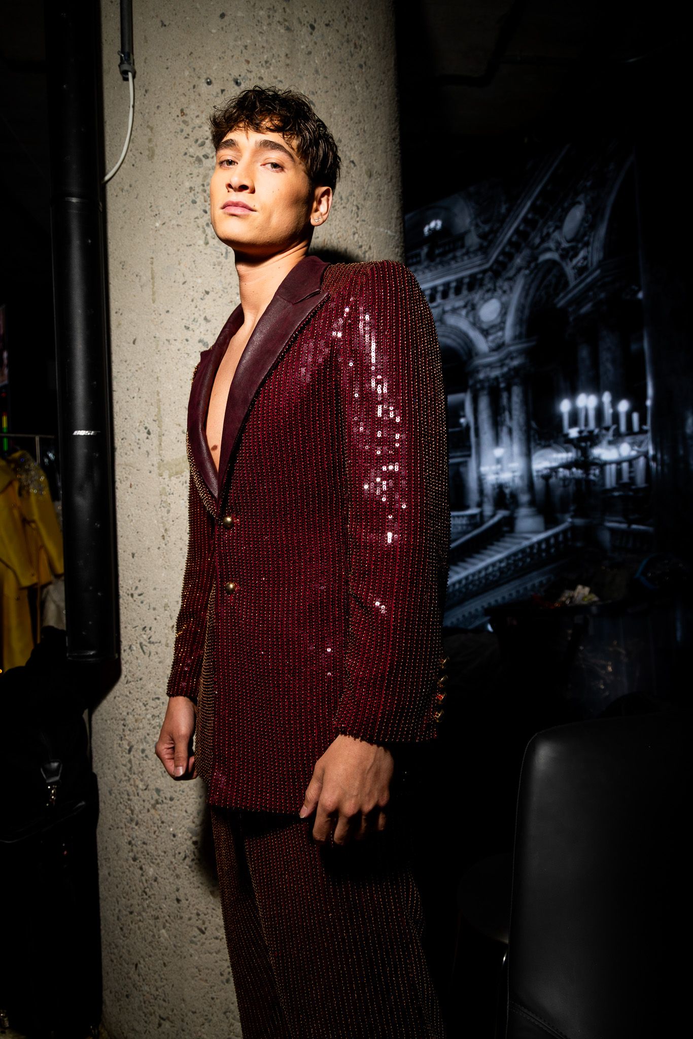 A fashion photoshoot featuring a burgundy sequined blazer in a dramatic dark setting.