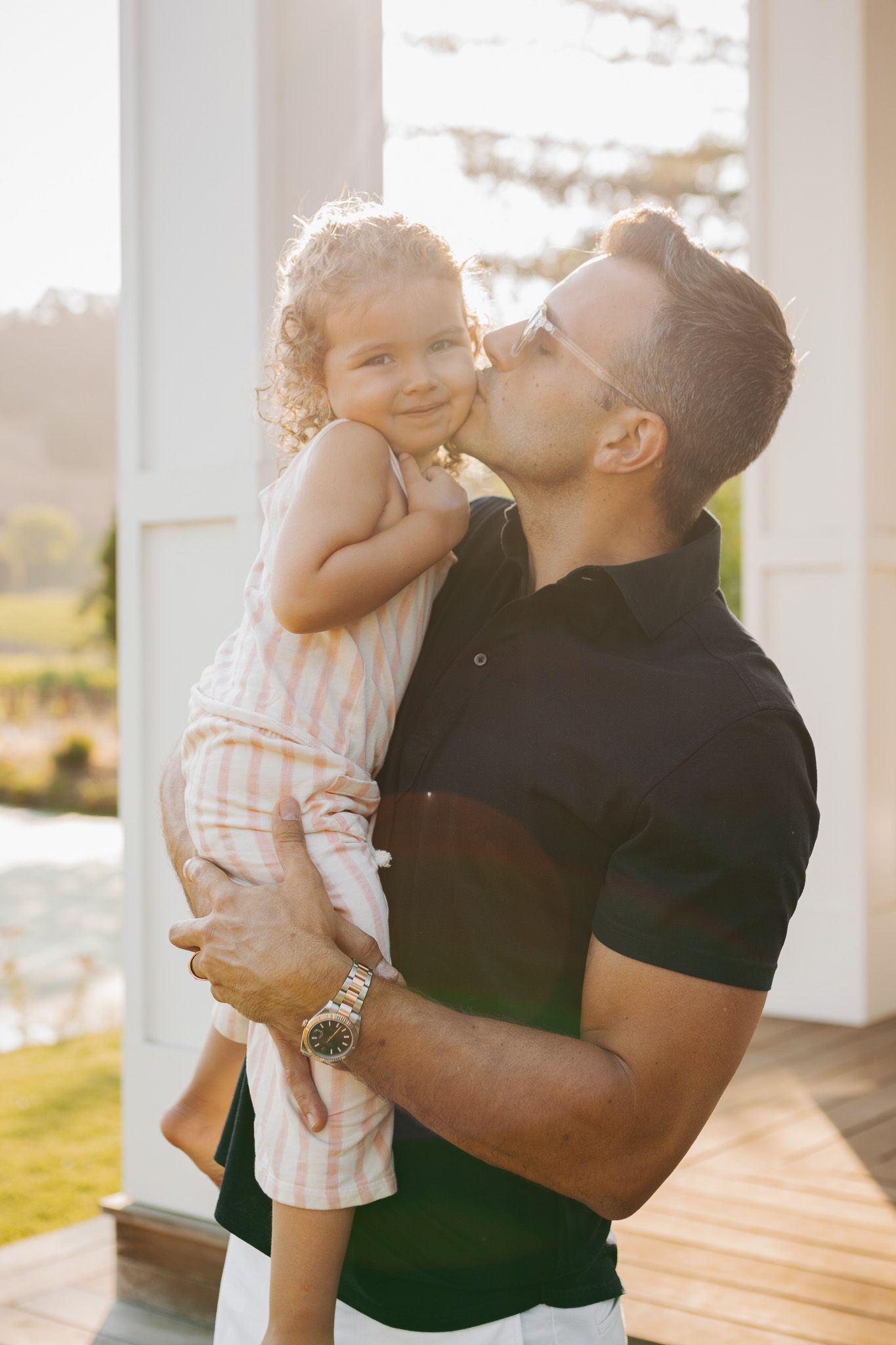 A tender moment shared between parent and child on a sunny porch with warm backlit glow.