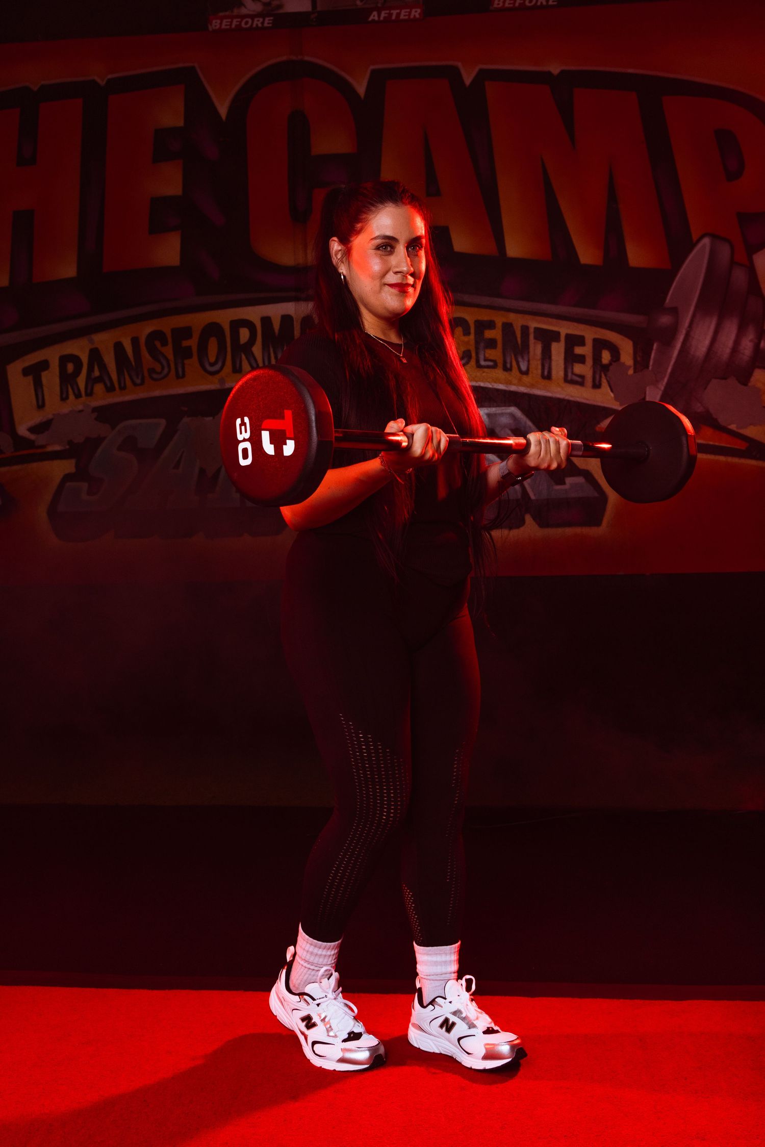 Athlete in black workout attire demonstrating proper form in a red-lit fitness studio.