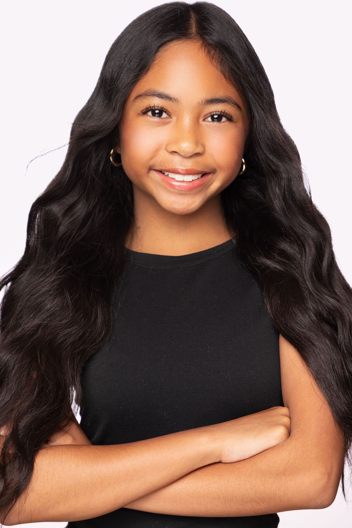 Professional portrait featuring long dark wavy hair, black top, and crossed arms against white background.