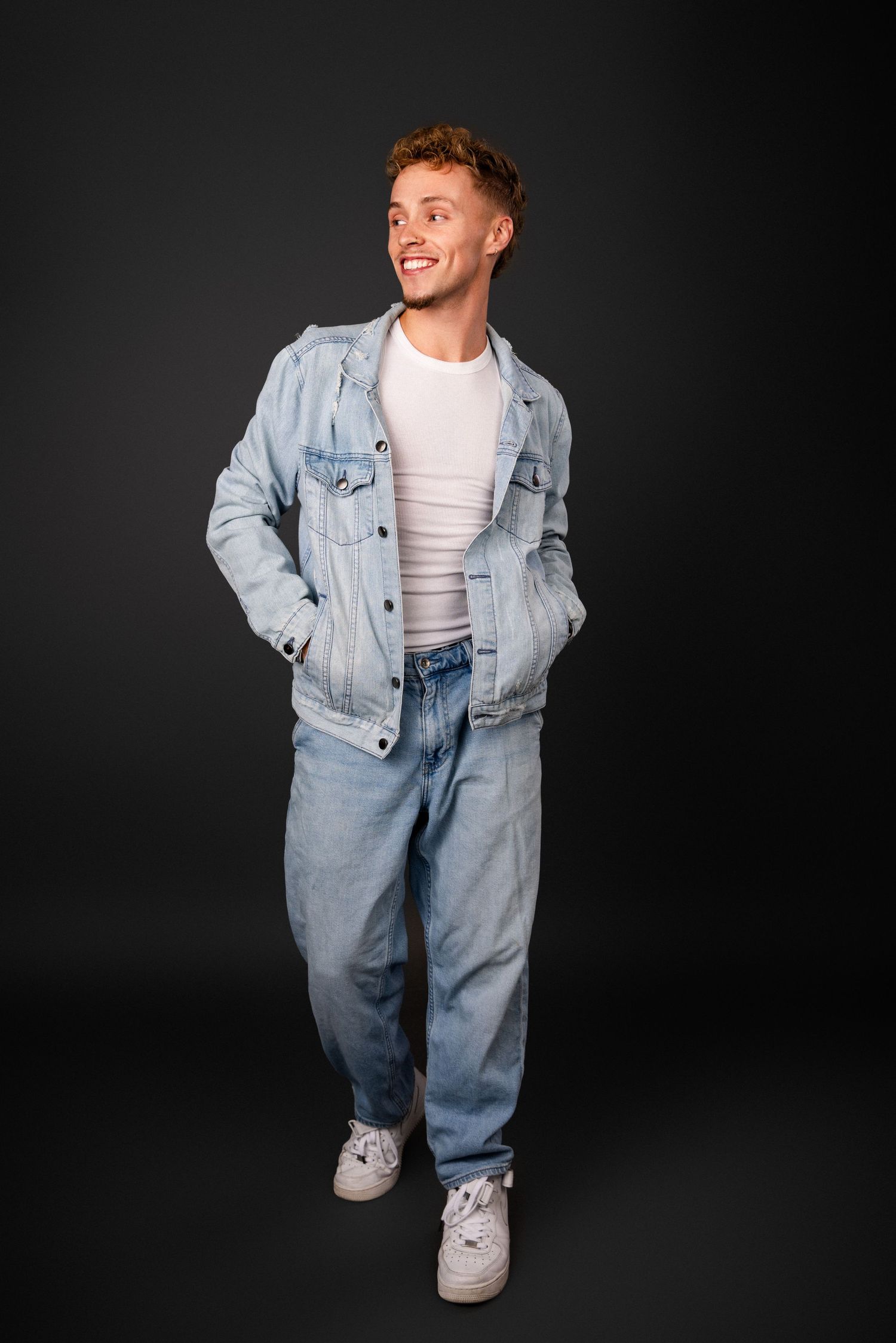 Studio model in oversized denim jacket and jeans poses playfully in four different positions against dark backdrop.